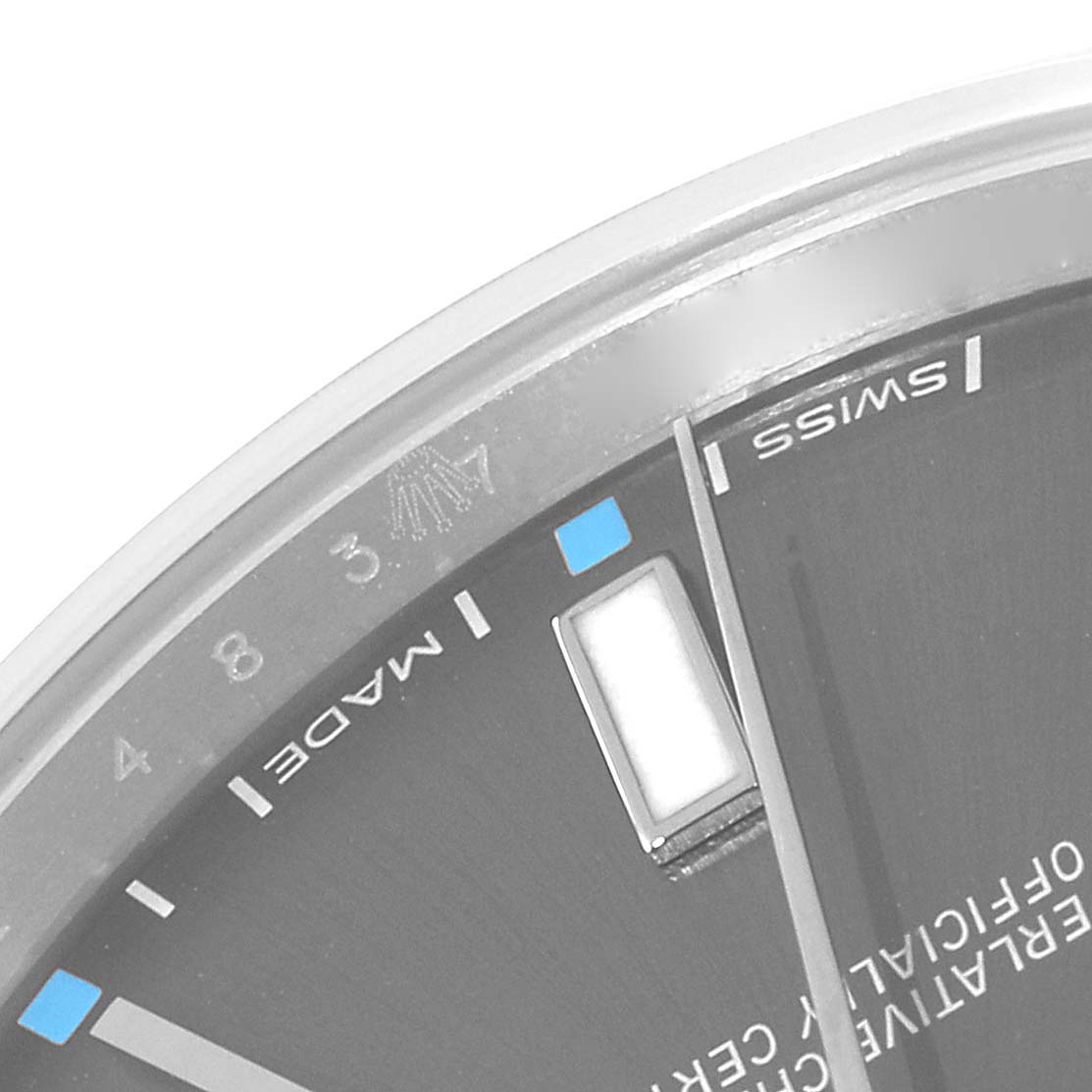 The image shows a close-up of the dial of a Rolex Oyster Perpetual 114300 Men's Stainless Steel Grey Dial 114300 Men's Stainless Steel Grey Dial, highlighting the markers and part of the minute hand.