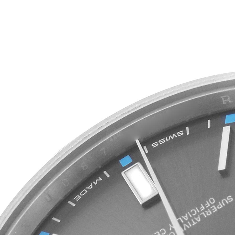 The image shows a close-up of the Rolex Oyster Perpetual 114300 Men's Stainless Steel Grey Dial watch dial, highlighting indices and partial branding details.