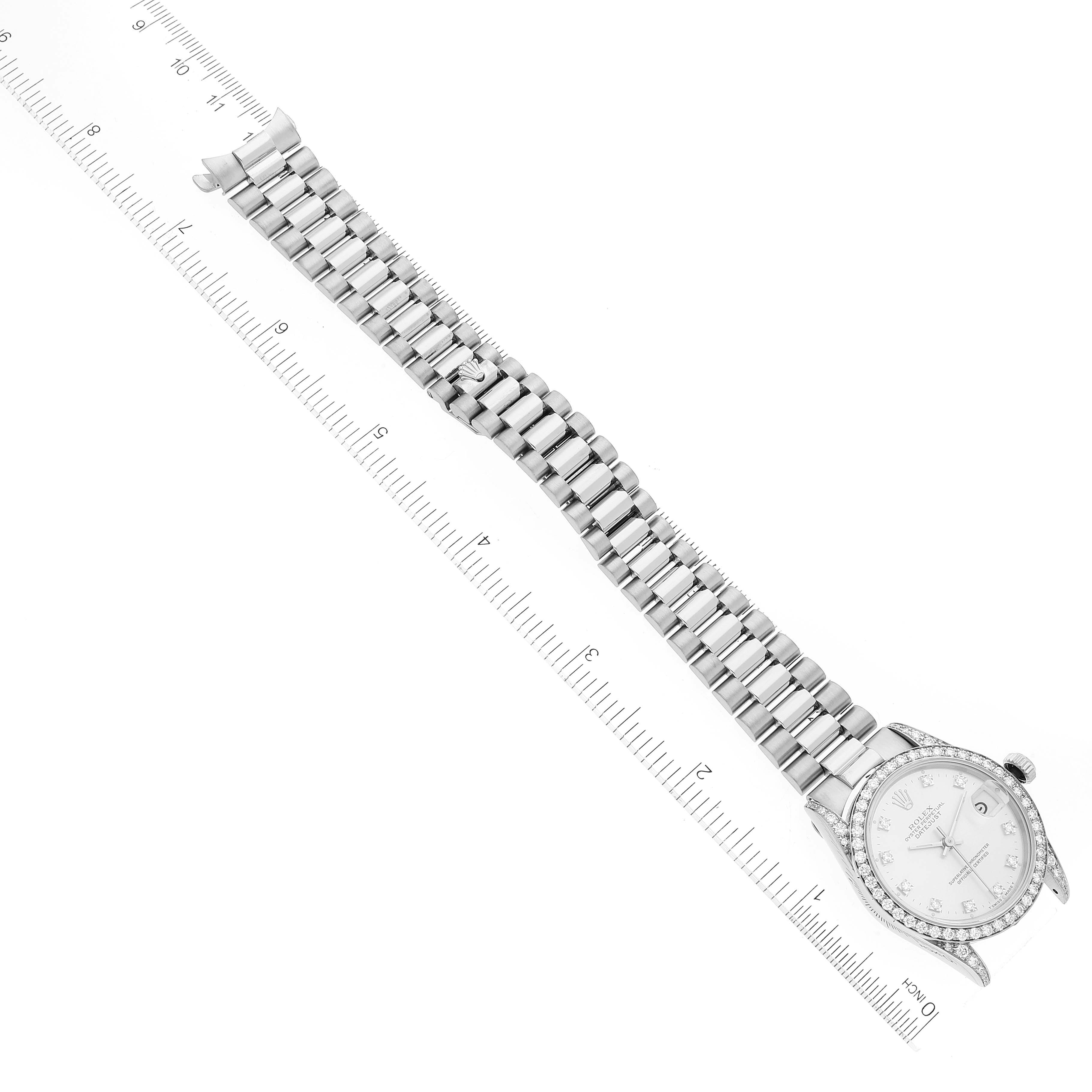 The Rolex President 68159 Women's White Gold Silver Dial 68159 Women's White Gold Silver Dial model watch is shown from a top-down angle, displaying the full bracelet, dial, and case beside a ruler.