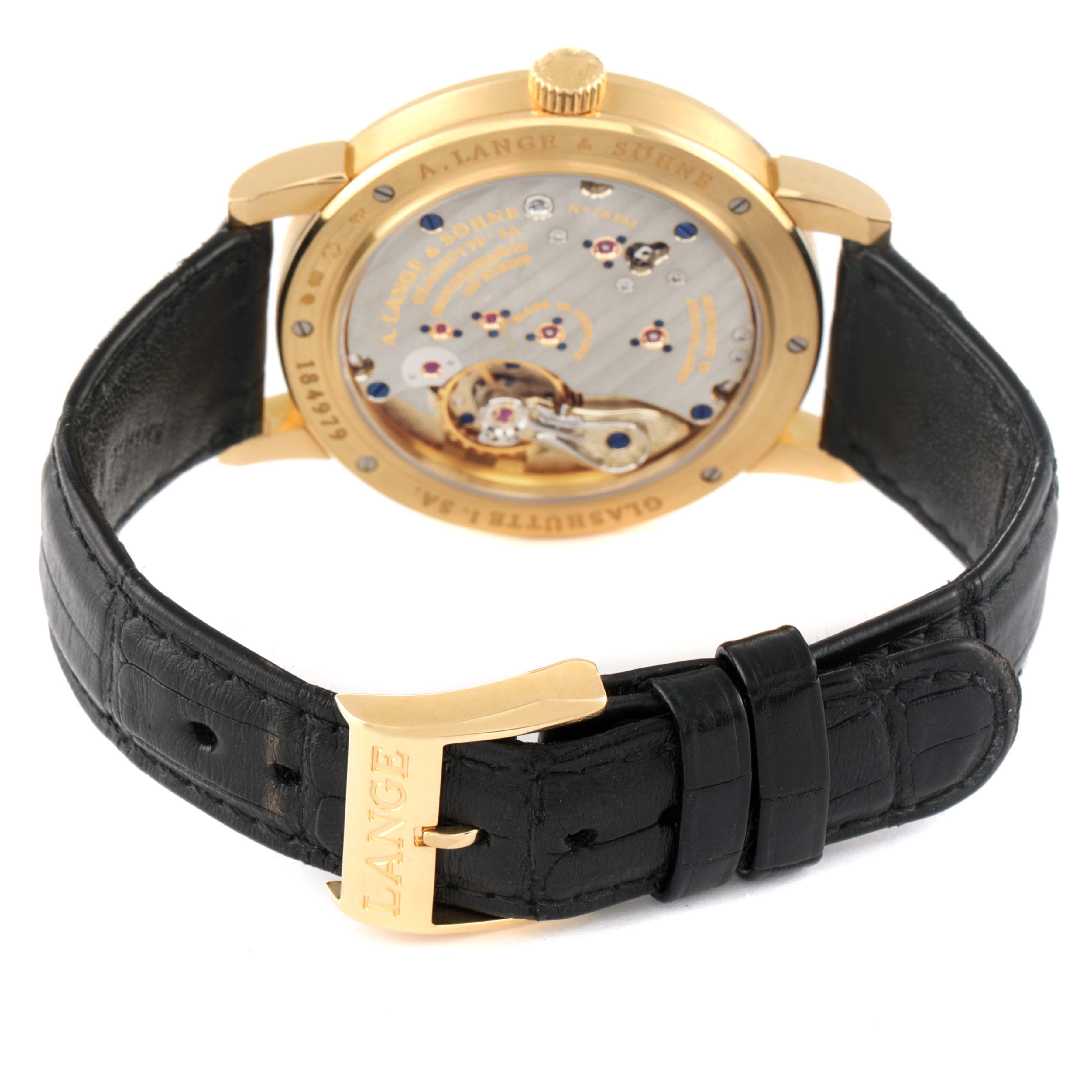 This image shows the back view of an A. Lange & Sohne 1815 233.021 Men's Yellow Gold Silver Dial watch, highlighting the movement mechanism and leather strap with gold buckle.