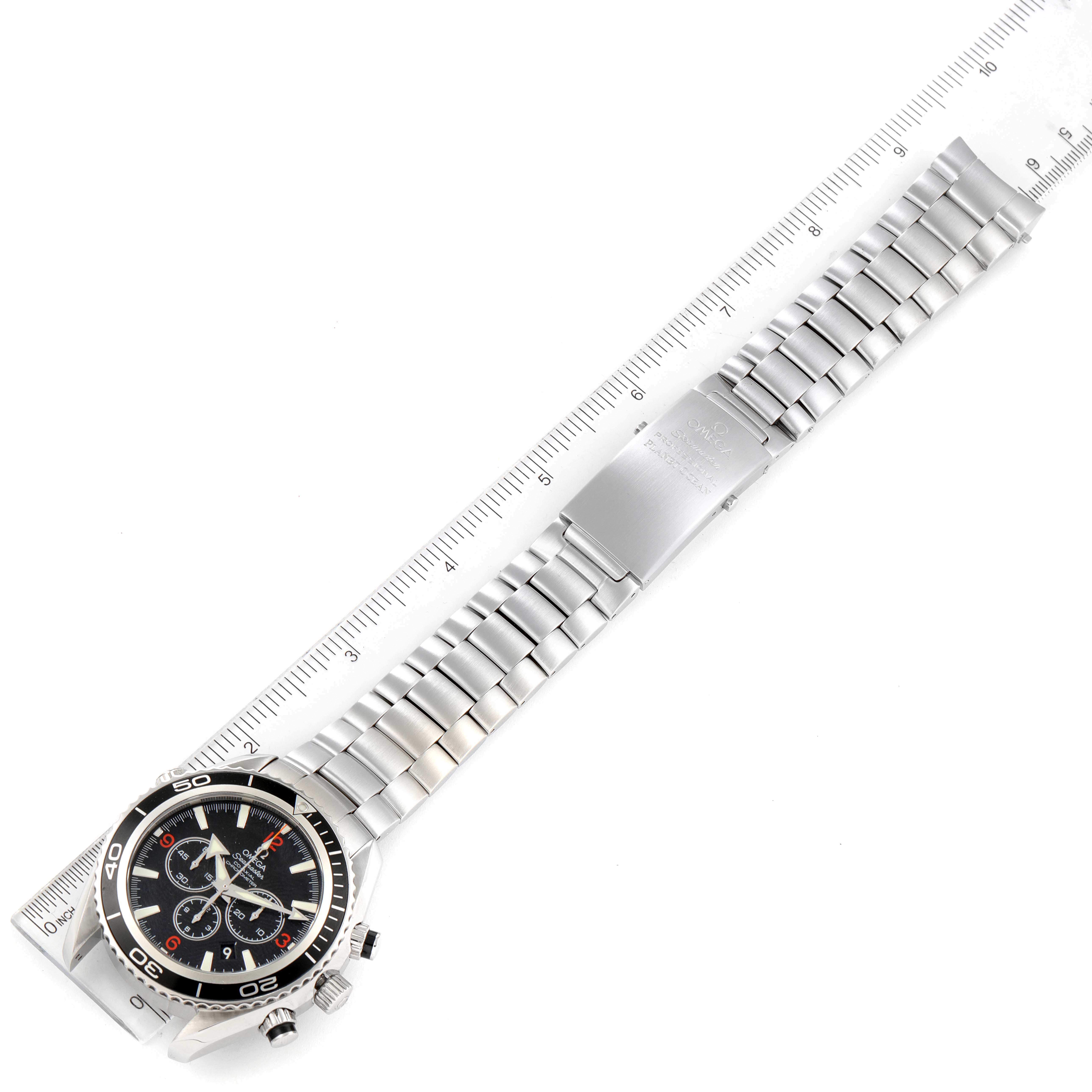 The Omega Planet Ocean 2210.51.00 Men's Stainless Steel Black Dial 2210.51.00 Men's Stainless Steel Black Dial watch is shown laying flat with its stainless steel bracelet and clasp visible, aligned next to a ruler.