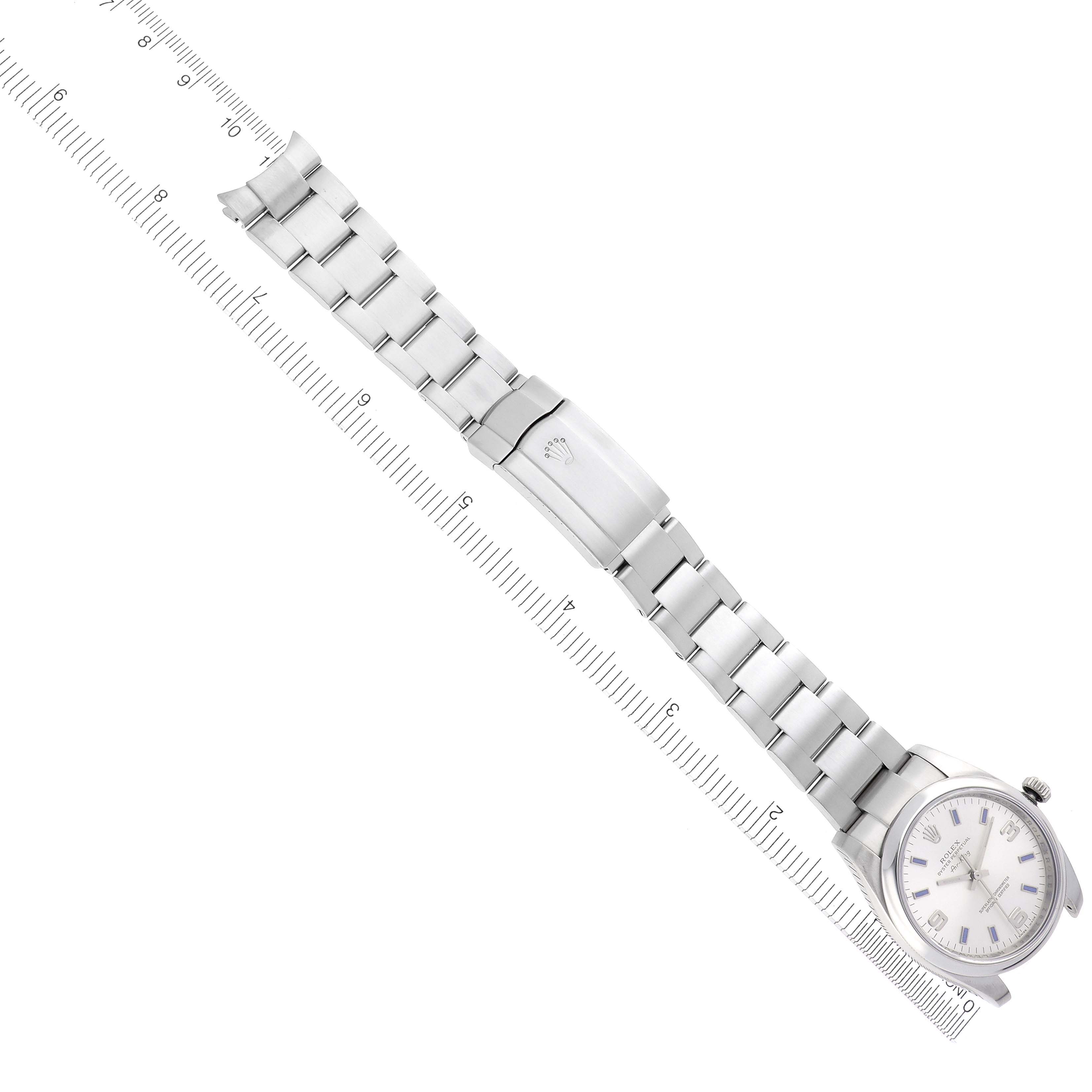 The Rolex Air-King 114200 Men's Stainless Steel Silver Dial 114200 Men's Stainless Steel Silver Dial watch is shown from a top view, displaying its bracelet, clasp, and face next to a ruler.