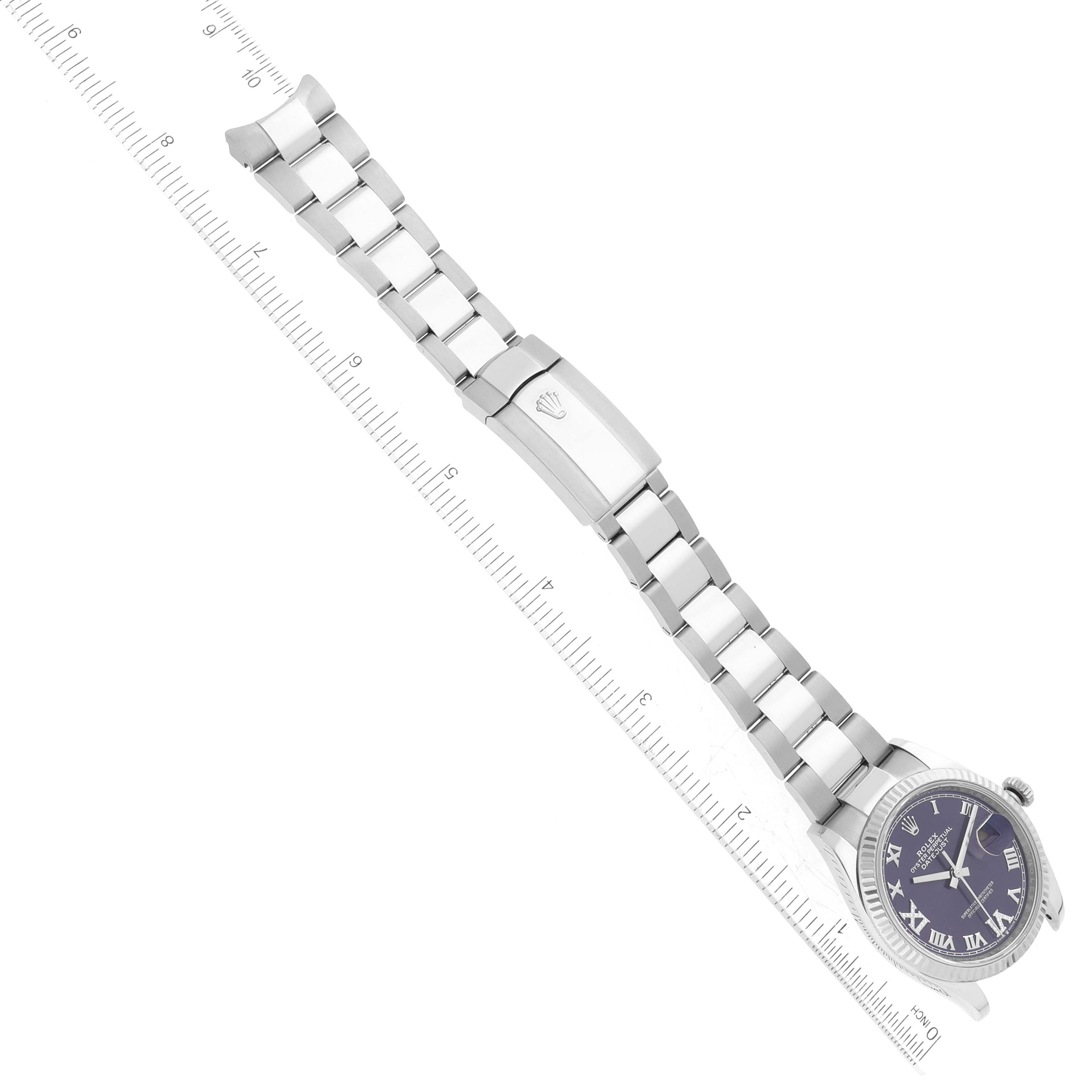 The image shows a top view of a Rolex Datejust 126234 Men's Stainless Steel Purple Dial 126234 Men's Stainless Steel Purple Dial watch with a purple dial and a stainless steel bracelet alongside a ruler.