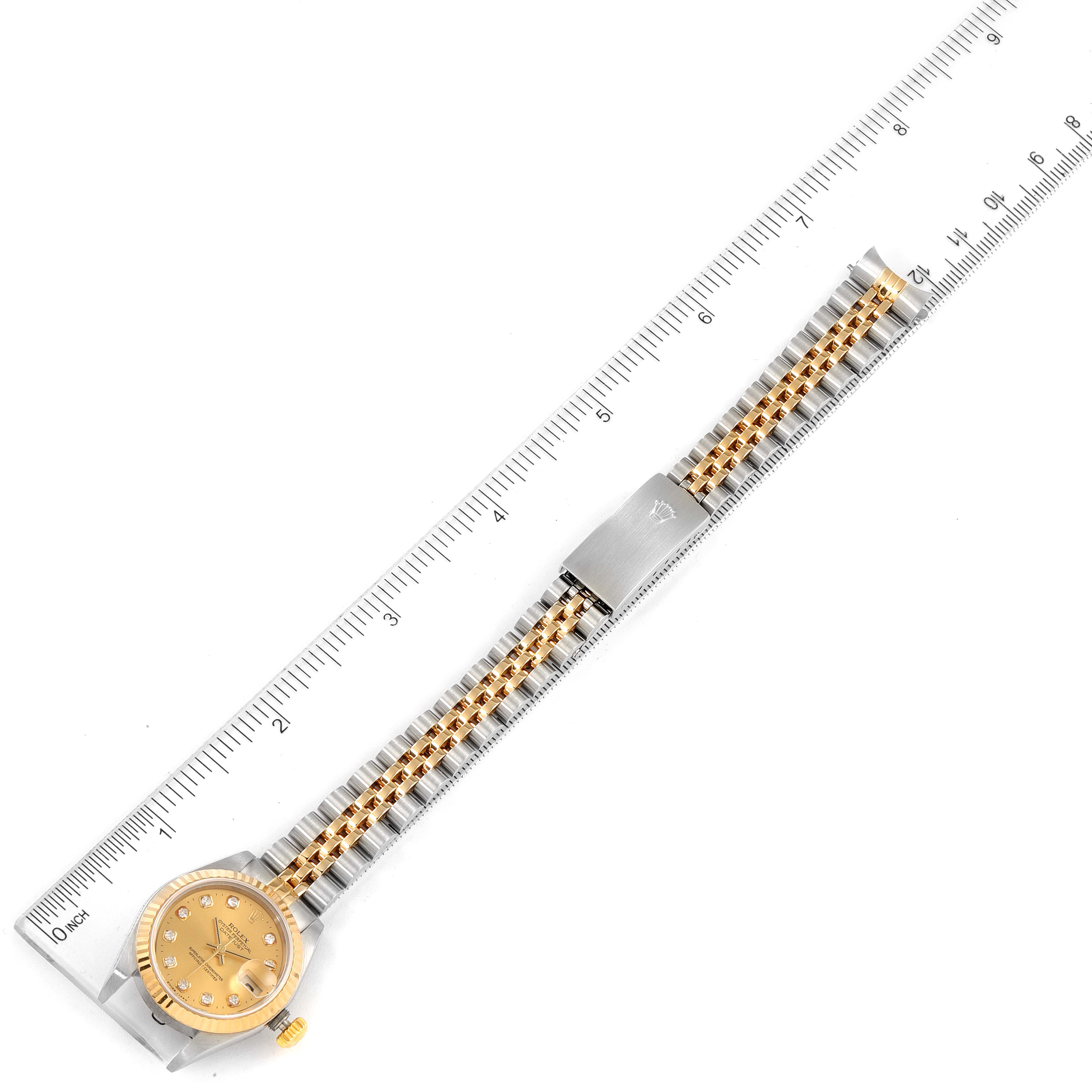 The image shows a top-down view of a Rolex Datejust 79173 Women
s Steel and Gold (two tone) Champagne Dial 79173 Women
s Steel and Gold (two tone) Champagne Dial watch with its gold and silver bracelet extended, beside a ruler.