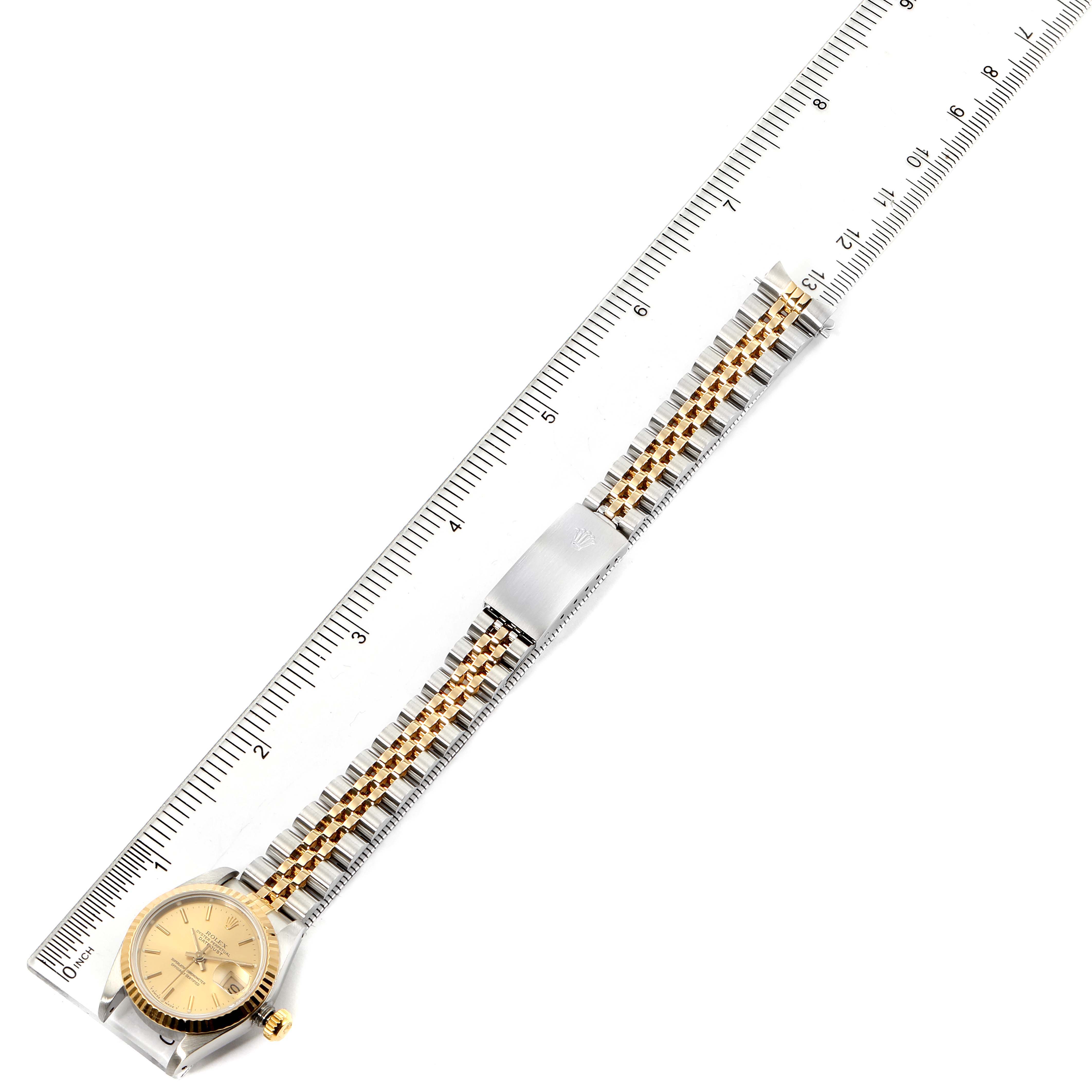 This image shows the Rolex Datejust 69173 Women's Steel and Gold (two tone) Champagne Dial 69173 Women's Steel and Gold (two tone) Champagne Dial watch placed next to a ruler, highlighting its band and face from a top-down angle.