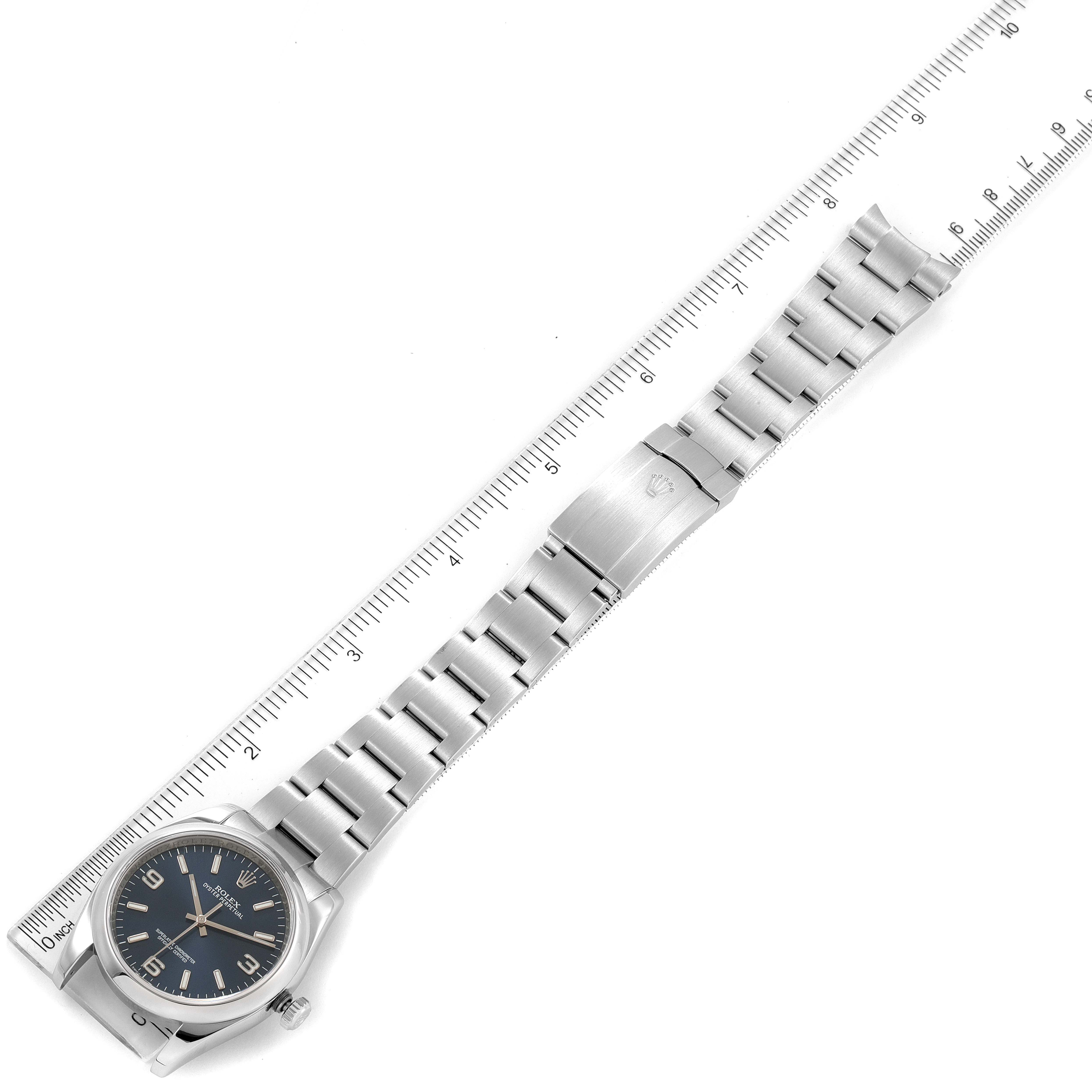 The image shows the Rolex Air-King 116000 Men's Stainless Steel Blue Dial 116000 Men's Stainless Steel Blue Dial watch positioned next to a ruler, displaying its face and metal bracelet from a bird's-eye view.