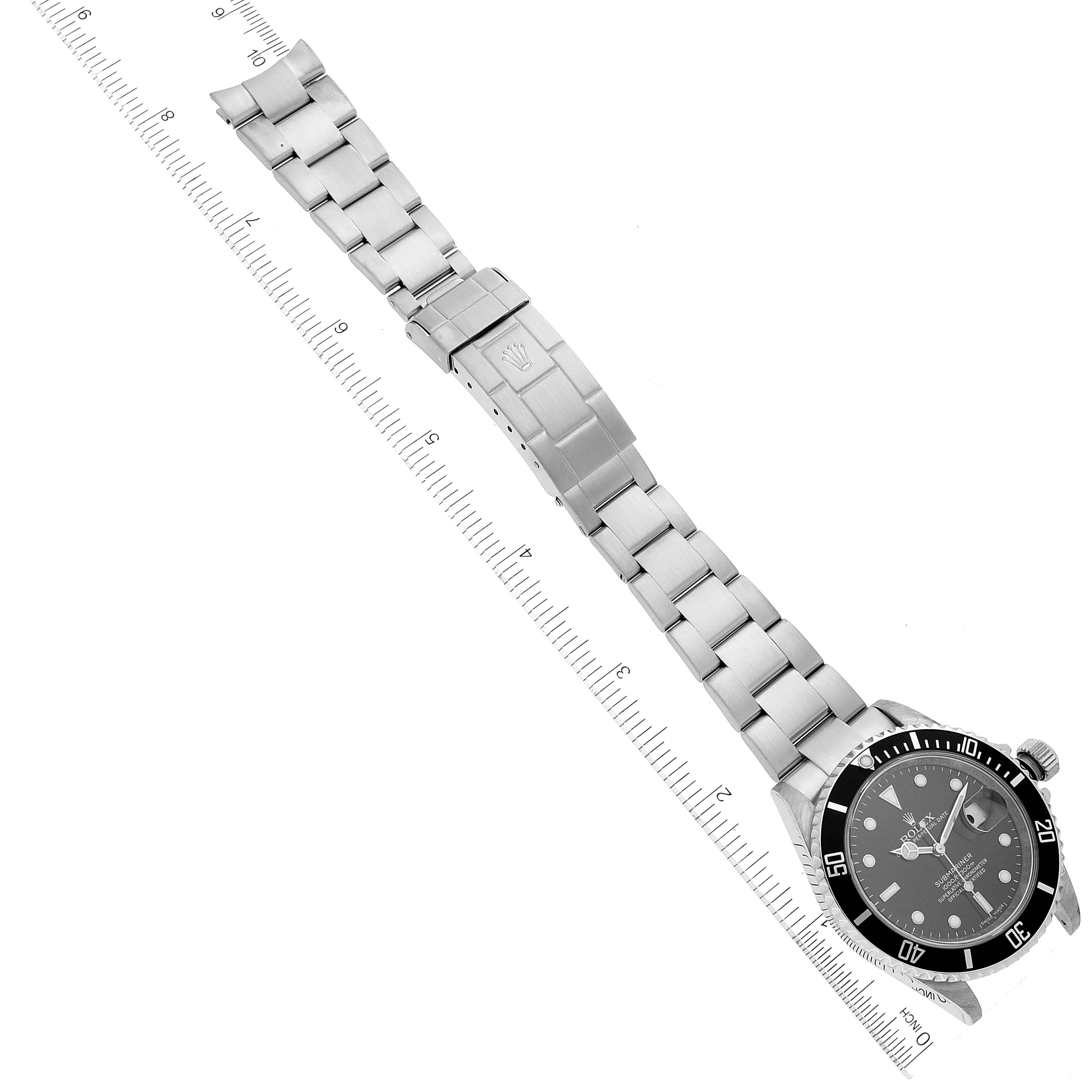 The image shows a top-down view of the Rolex Submariner 16610 Men's Stainless Steel Black Dial 16610 Men's Stainless Steel Black Dial watch, highlighting its face, bezel, bracelet, and clasp against a ruler.