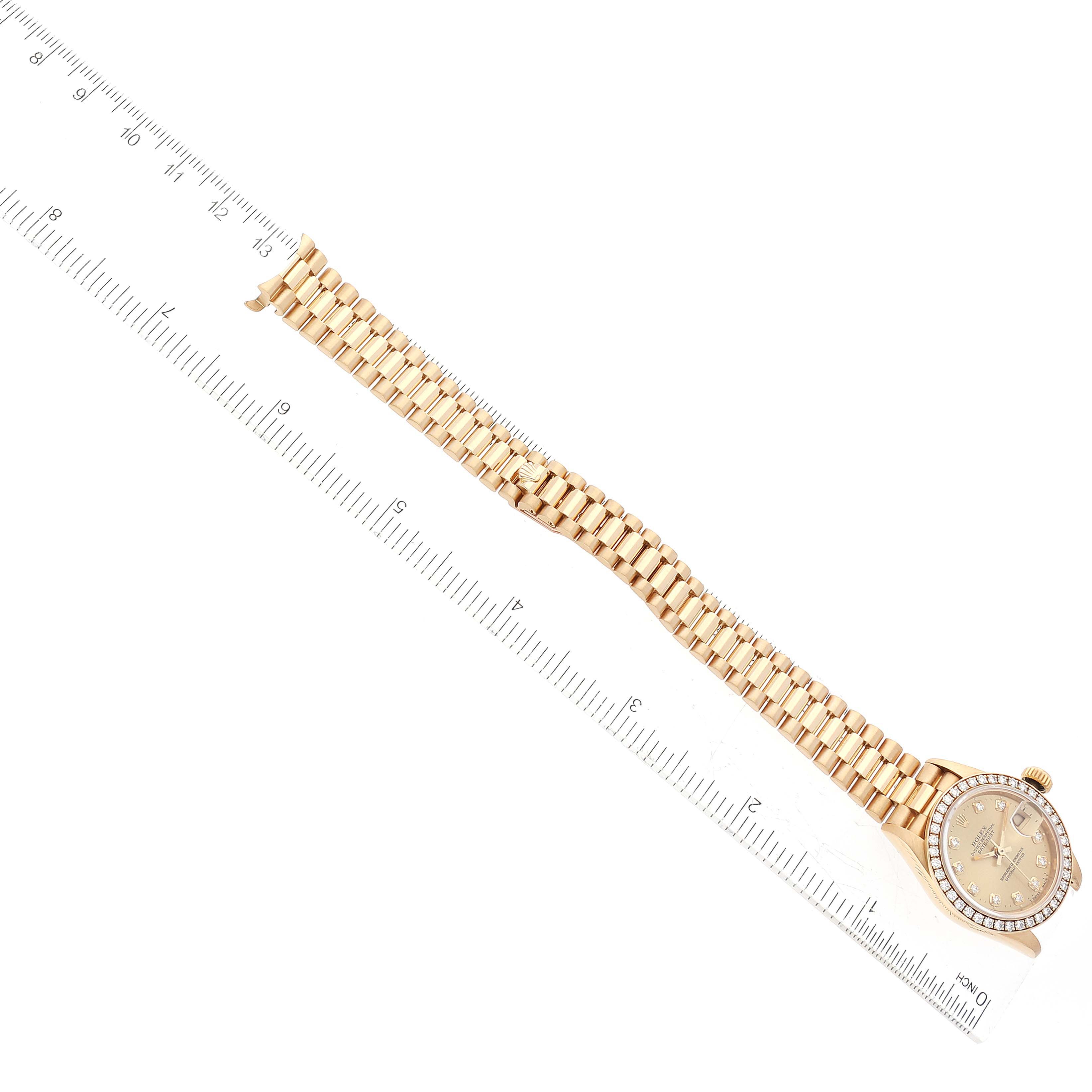 The Rolex President 69138G Women
s Yellow Gold Champagne Dial 69138G Women
s Yellow Gold Champagne Dial model watch is shown from a top view, displaying its face and entire gold bracelet alongside a ruler for scale.