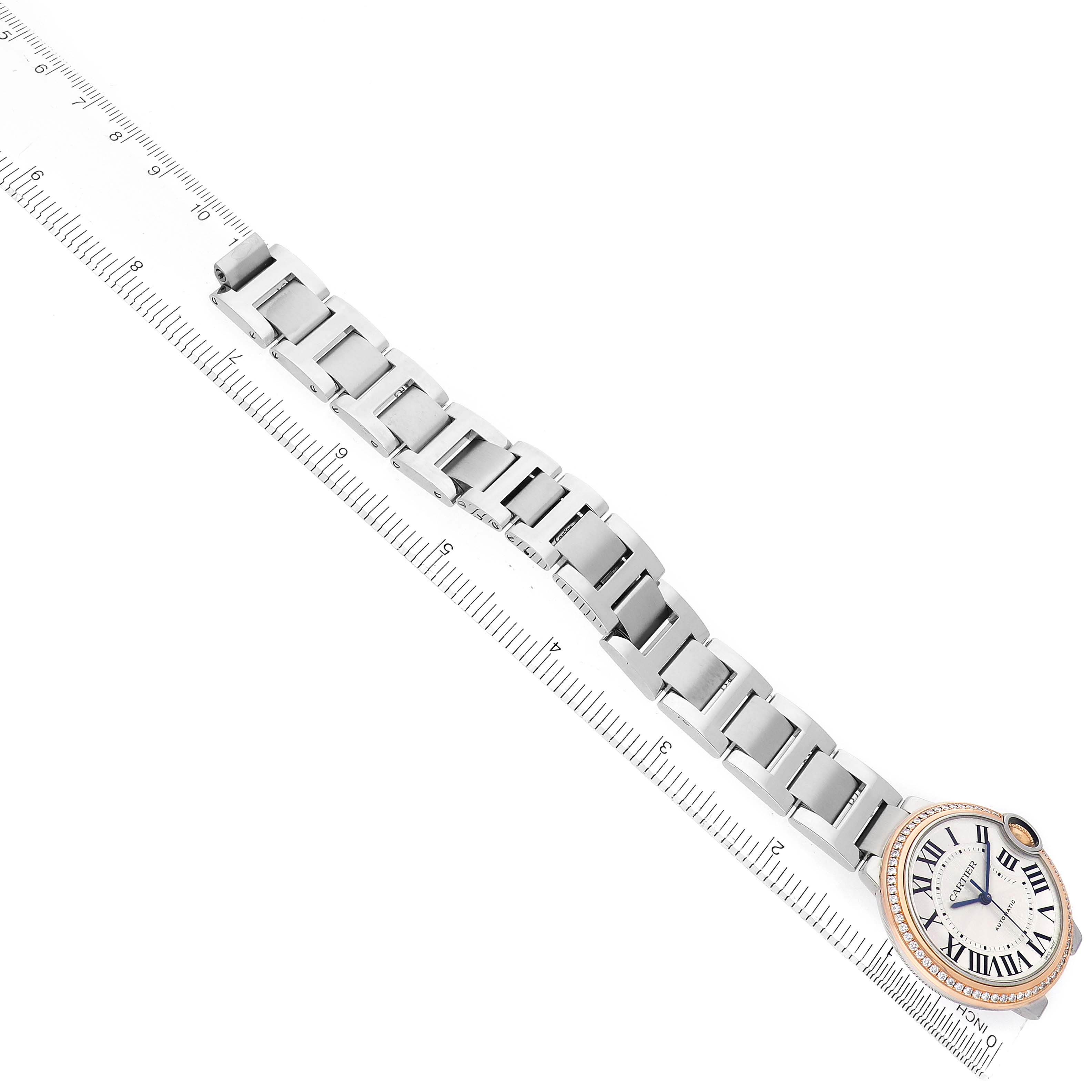 The Cartier Ballon Bleu WE902081 Women's Steel and Gold (two tone) Silver Dial watch is shown in a top-down angle, highlighting the face, bezel, and full bracelet next to a ruler.
