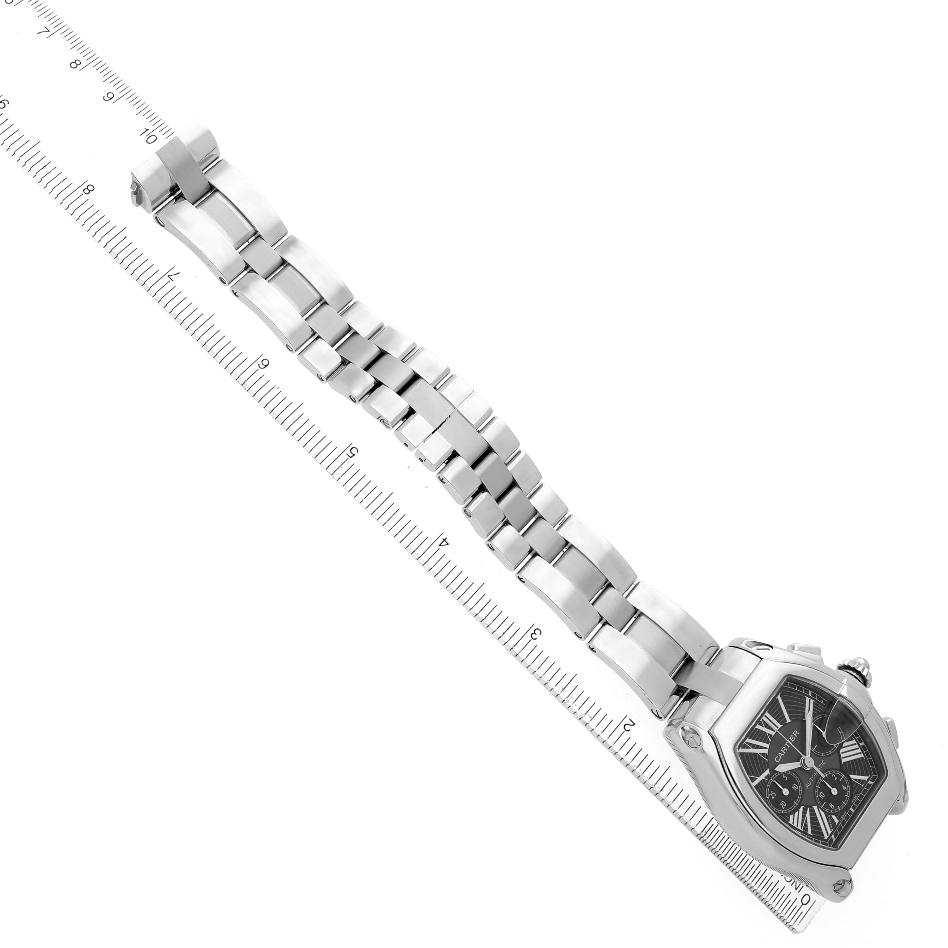 The Cartier Roadster W62020X6 Men's Stainless Steel Black Dial watch is shown from an overhead angle, with a focus on the full bracelet and the case alongside a ruler.