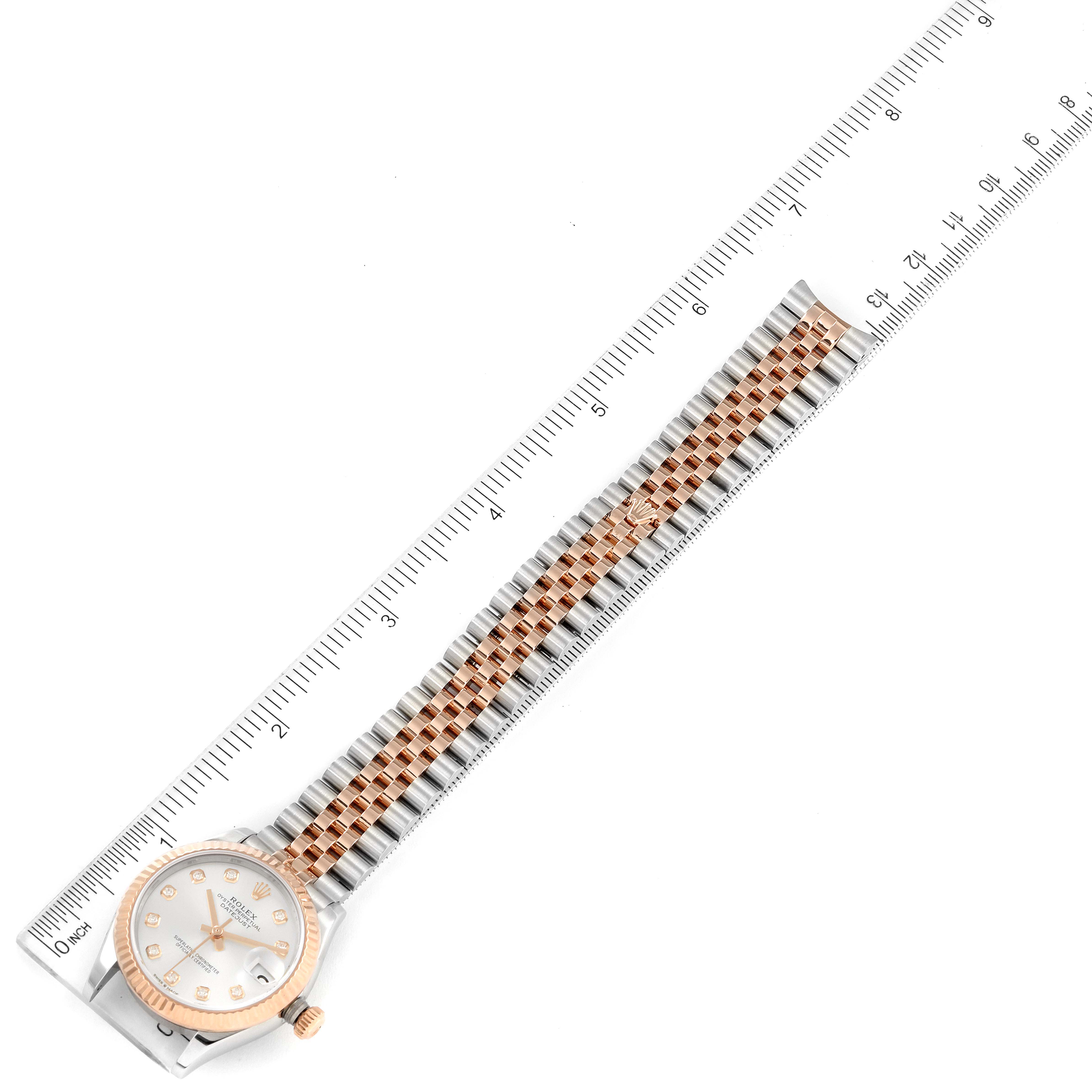 The image shows a Mid-Size Rolex watch, angled flat, displaying the face, bezel, and bracelet next to a ruler for measurement.