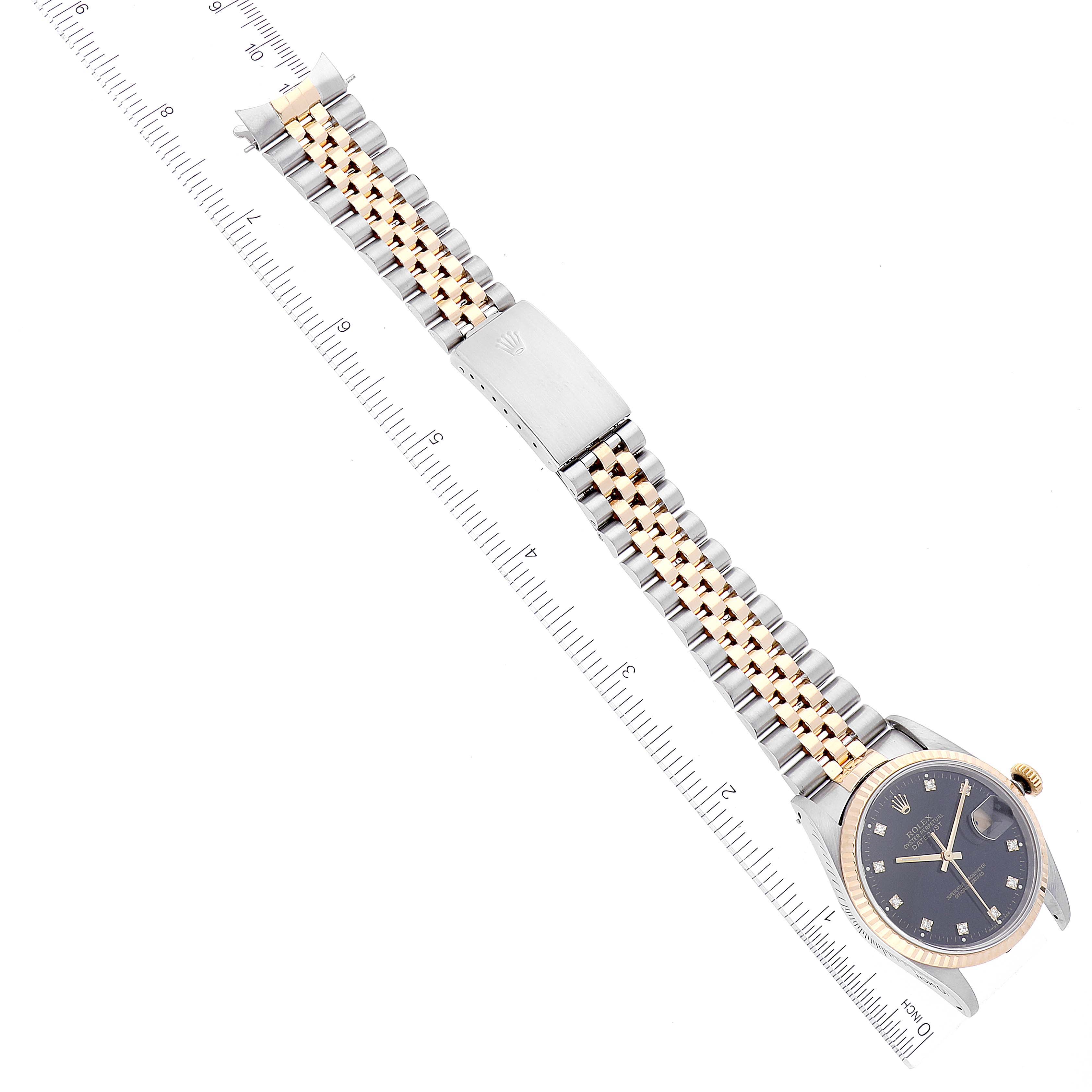 The image shows a top-down view of a Rolex Datejust 16233 Men's Steel and Gold (two tone) Black Dial 16233 Men's Steel and Gold (two tone) Black Dial watch, including the face, bezel, band, and clasp alongside a ruler.