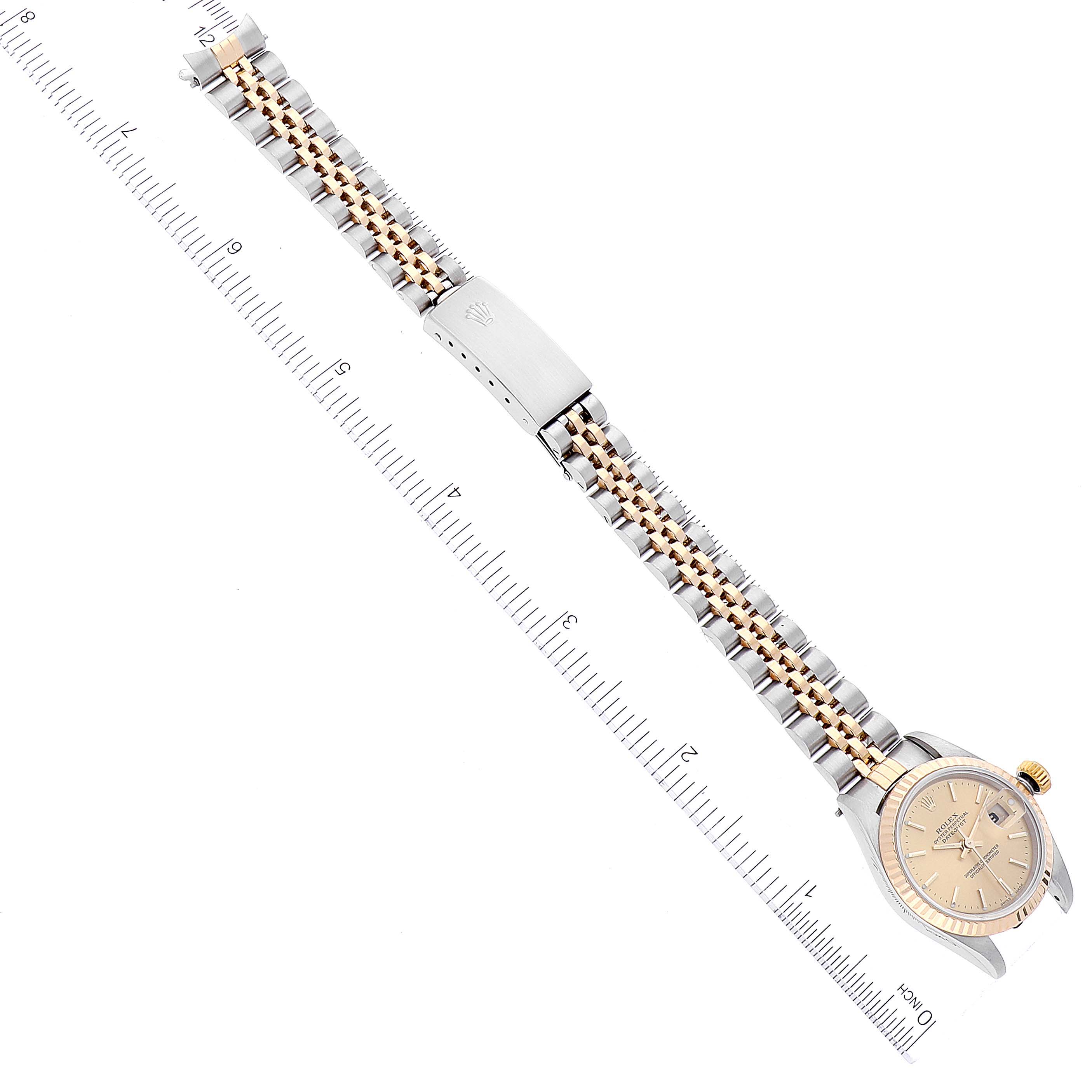 The Rolex Datejust 79173 Women's Steel and Gold (two tone) Champagne Dial 79173 Women's Steel and Gold (two tone) Champagne Dial watch is shown in a top-down view, displaying its full bracelet, clasp, and face against a ruler backdrop.