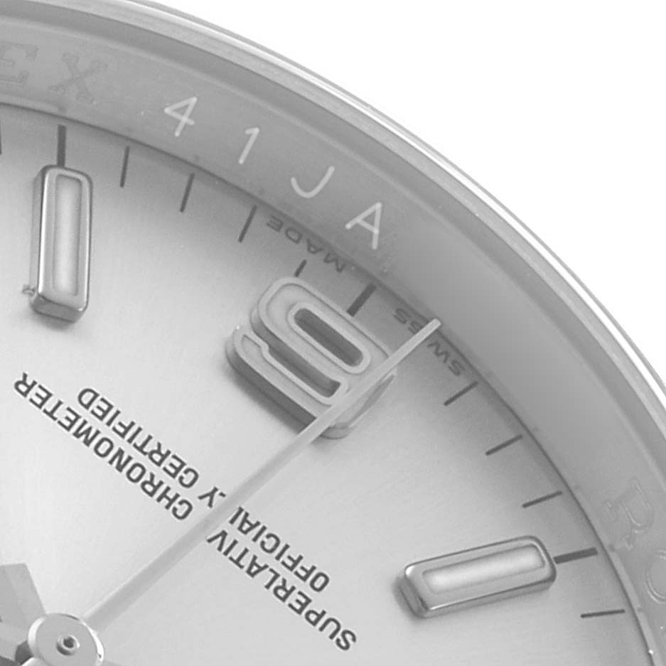 The image shows a close-up of the dial on a Rolex Oyster Perpetual 116000 Men's Stainless Steel Silver Dial watch, focusing on the "9" hour marker and text details.