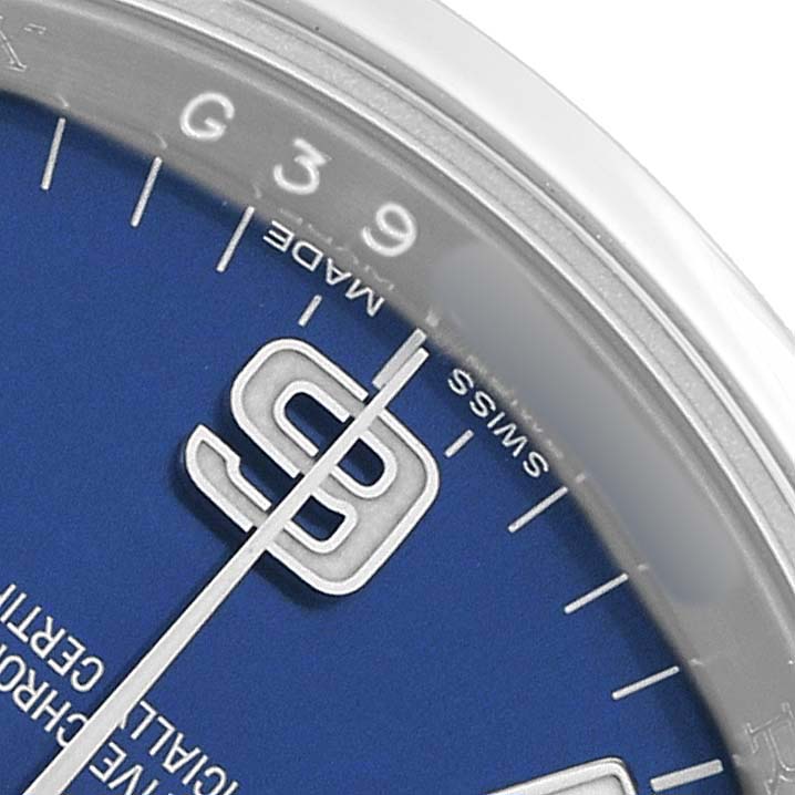 The image shows a close-up of the dial of a Rolex Oyster Perpetual 116000 Men's Stainless Steel Blue Dial watch, featuring the watch face, hour markers, and hands.