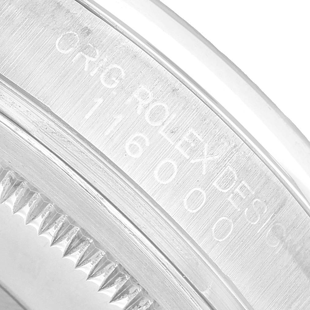 The image shows a close-up of the edge of a Rolex Oyster Perpetual 116000 Men's Stainless Steel Blue Dial watch, focusing on the engraved bezel and case.