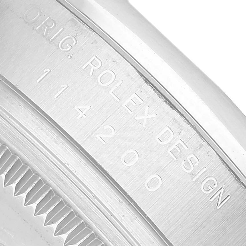 The image shows a close-up of the side of the Rolex Oyster Perpetual 114200 Men's Stainless Steel Silver Dial watch, highlighting the engraved design and model number.