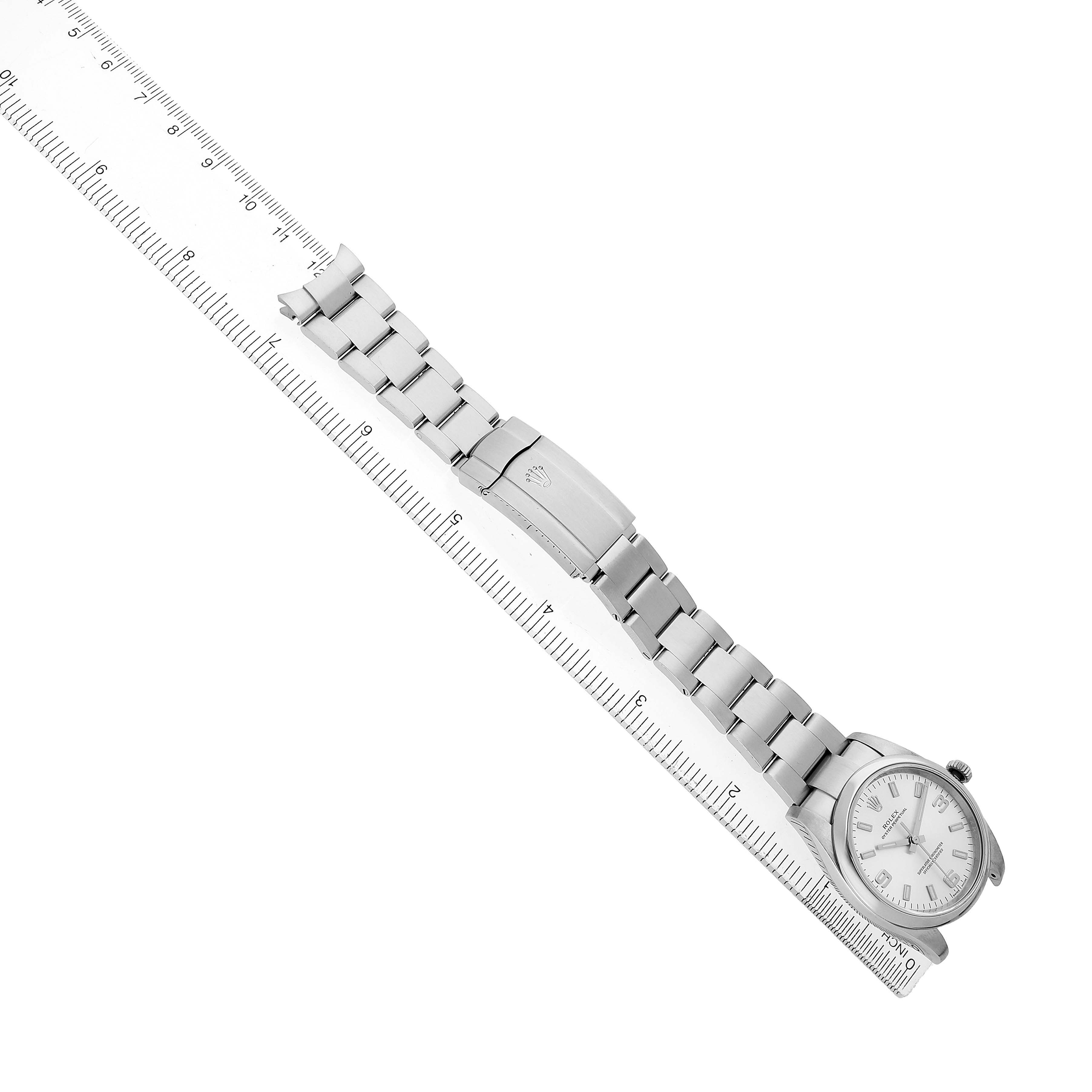 The image shows a Rolex Oyster Perpetual 114200 Men's Stainless Steel Silver Dial watch laid flat with its bracelet alongside a ruler, displaying the dial and clasp.