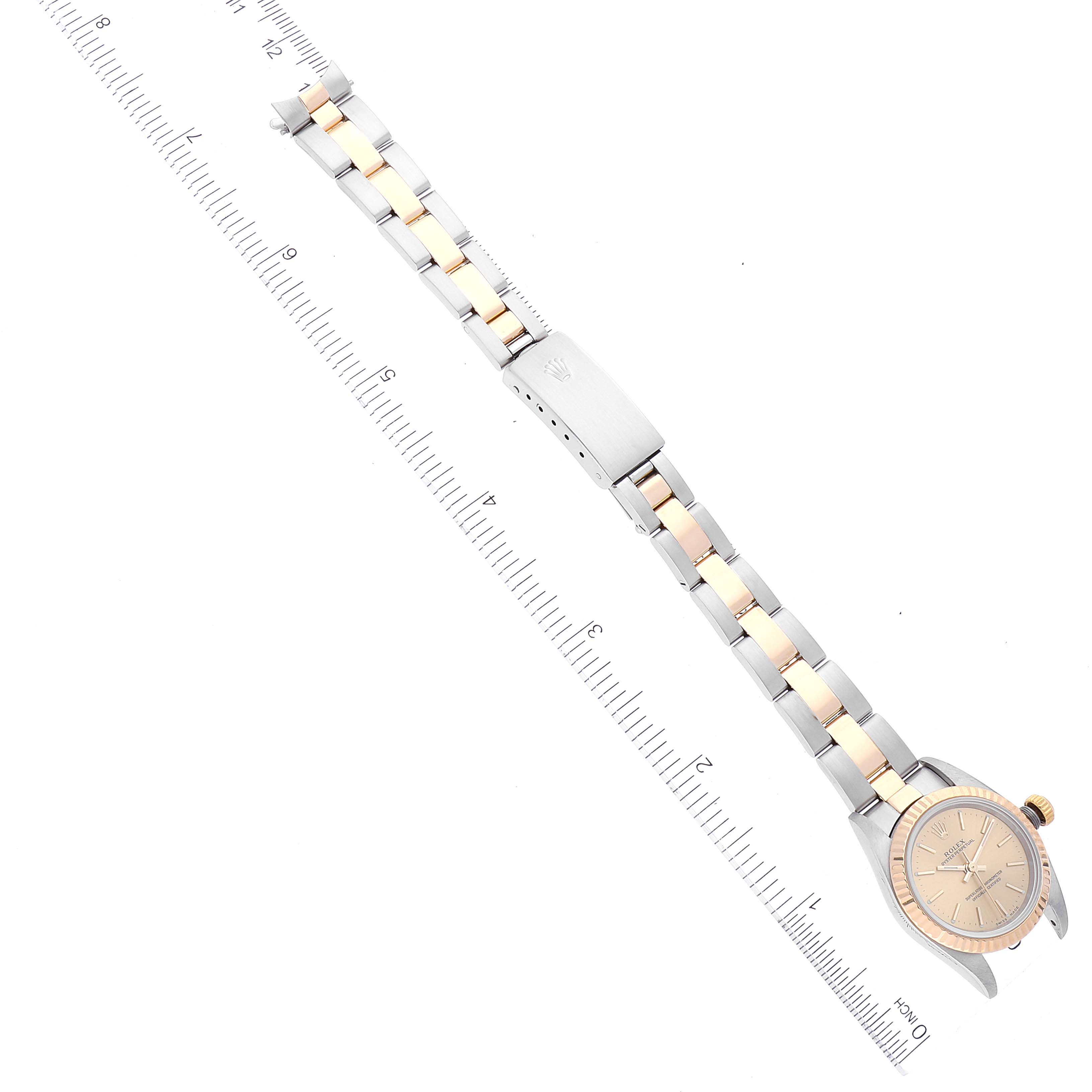 The image shows the full length of the Rolex Oyster Perpetual 76193 Women's Steel and Gold (two tone) Champagne Dial 76193 Women's Steel and Gold (two tone) Champagne Dial watch, including the face and the two-tone bracelet, laid alongside a ruler.