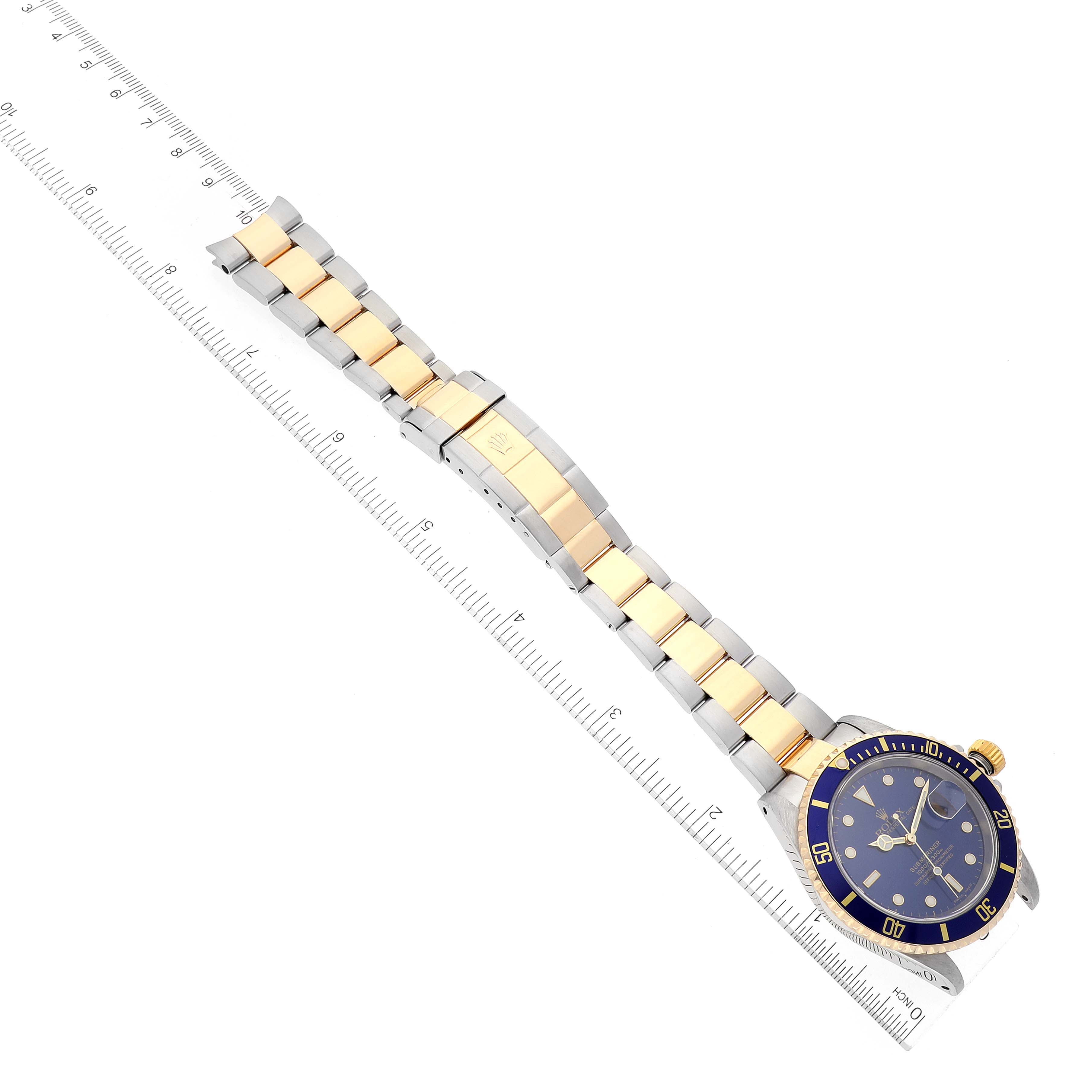 This image shows a Rolex Submariner 16613 Men's Steel and Gold (two tone) Blue Dial 16613 Men's Steel and Gold (two tone) Blue Dial watch, laid flat with the dial visible and a metal bracelet aligned next to a ruler for scale.