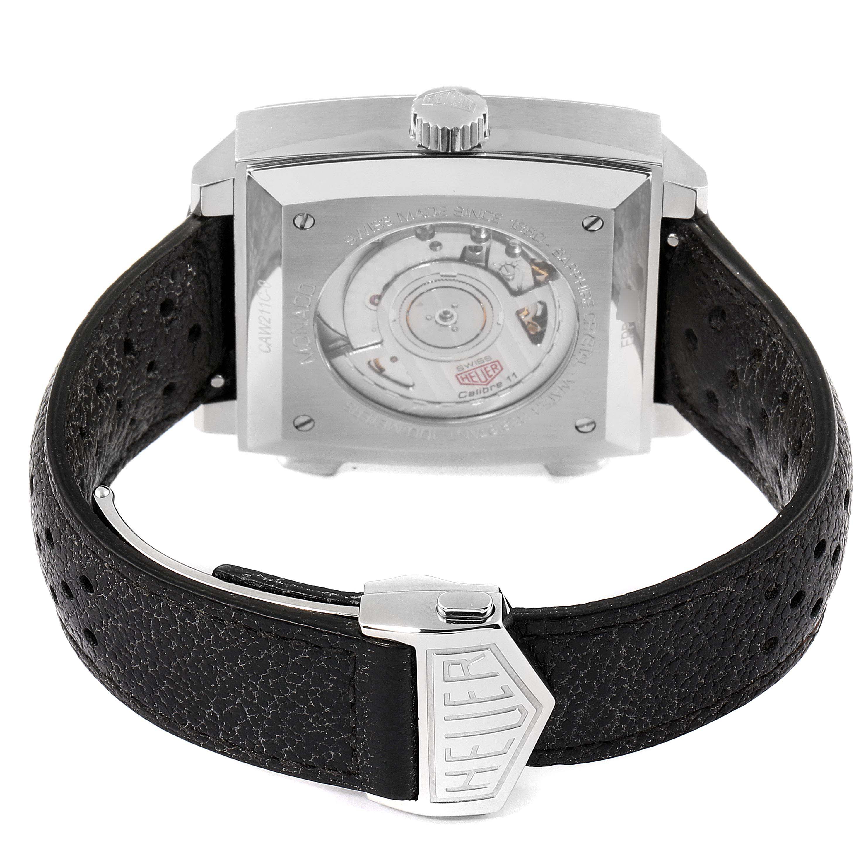The image shows the back view of the Tag Heuer Monaco watch, highlighting its movement and leather strap with a Heuer-branded clasp.