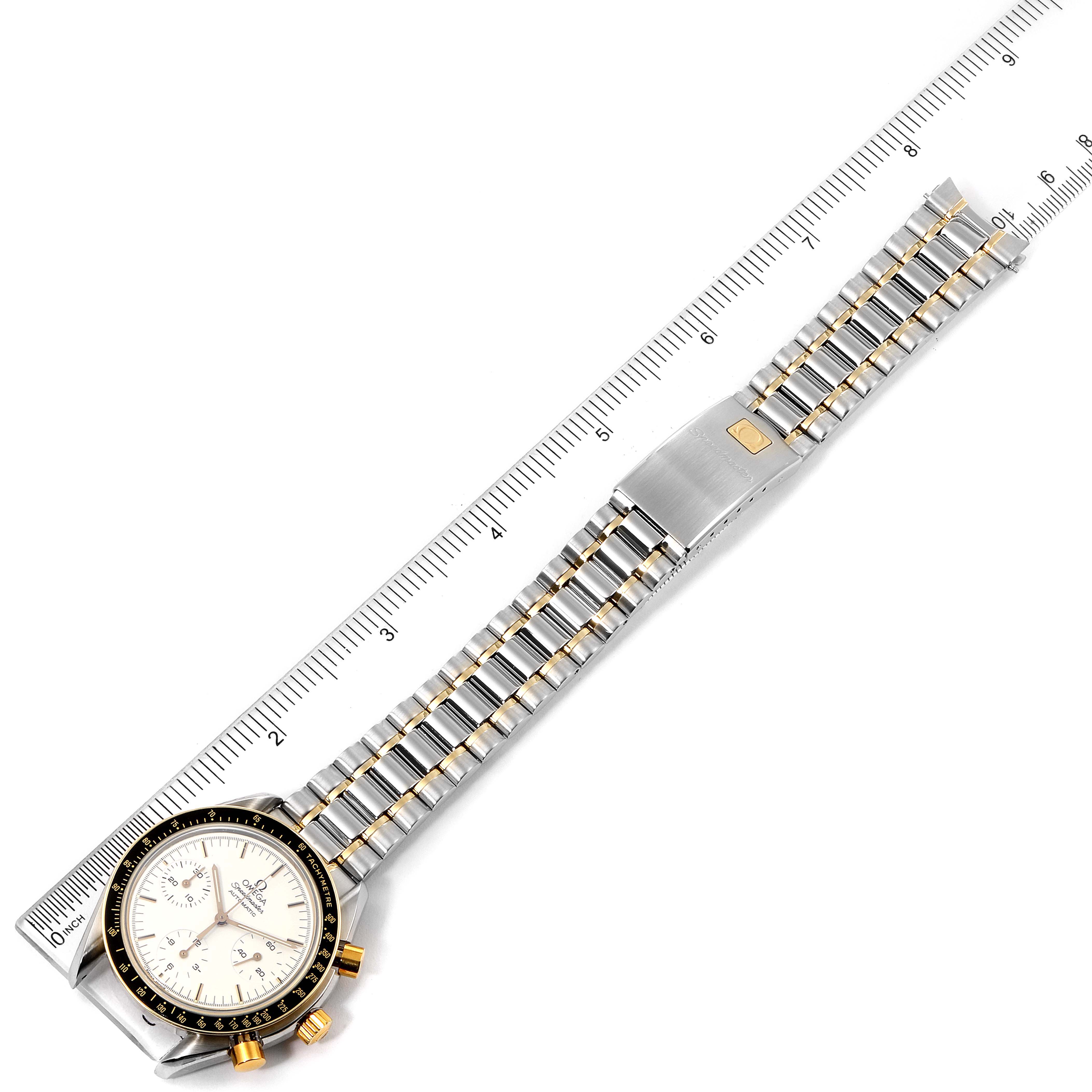This image shows an overhead view of an Omega Speedmaster 3310.20.00 Men's Steel and Gold (two tone) White Dial 3310.20.00 Men's Steel and Gold (two tone) White Dial watch with its bracelet and clasp, alongside a measuring scale.