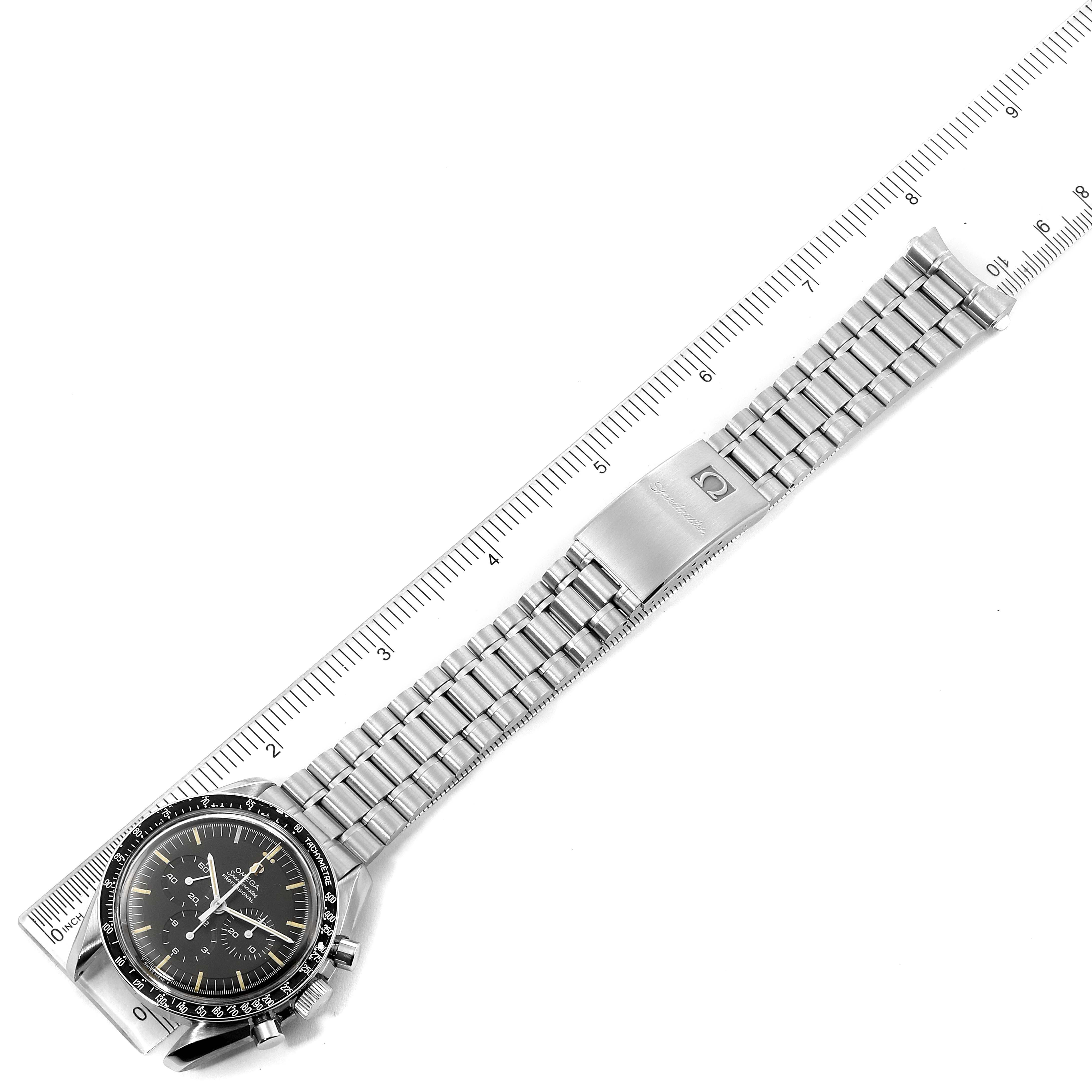 The image shows an Omega Speedmaster 145.022 Men's Stainless Steel Black Dial 145.022 Men's Stainless Steel Black Dial watch laid flat against a ruler, displaying its face and full bracelet.