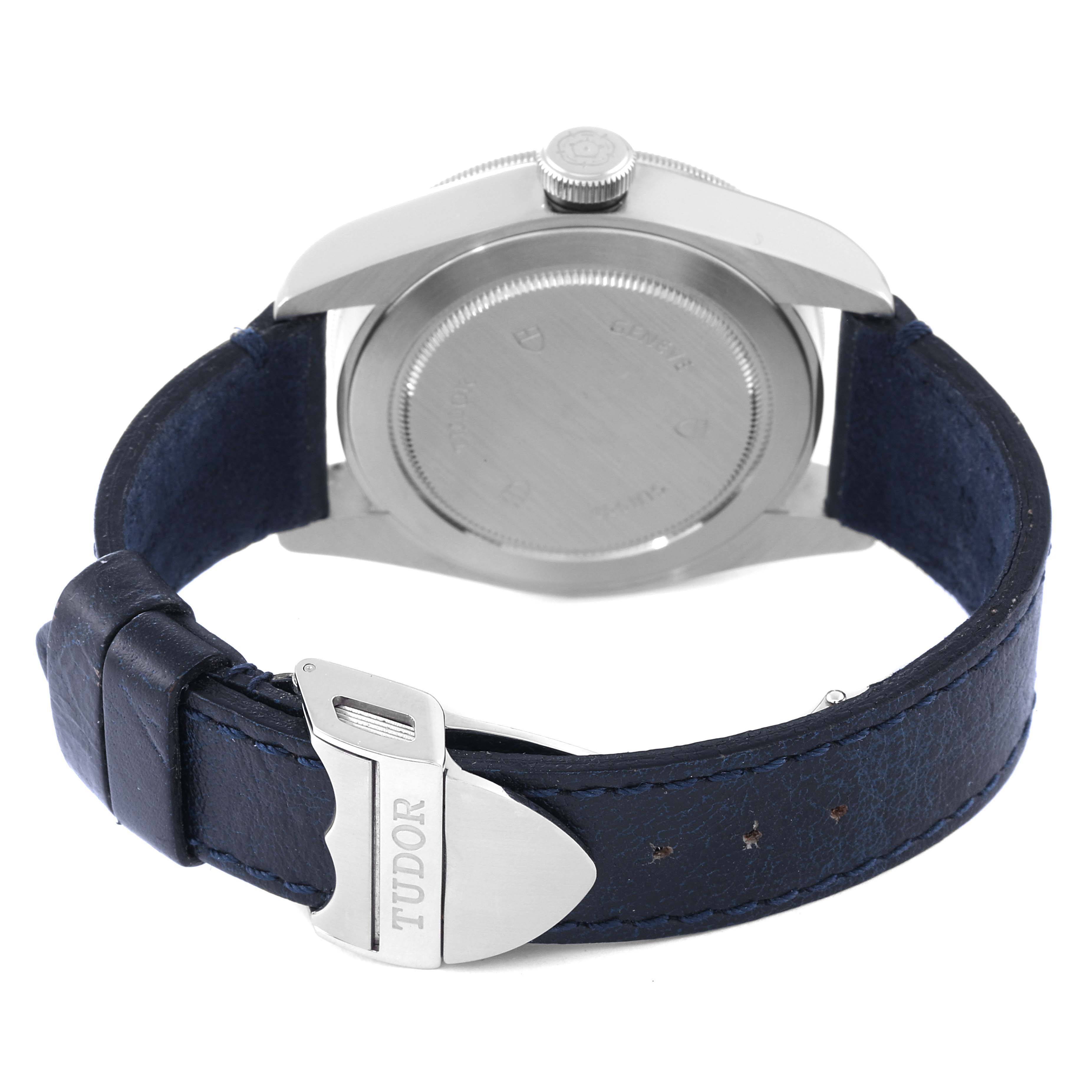 The image shows the back of a Tudor Heritage Black Bay 79220 Men's Stainless Steel Black Dial 79220 Men's Stainless Steel Black Dial watch and its blue leather strap with a Tudor-branded buckle.