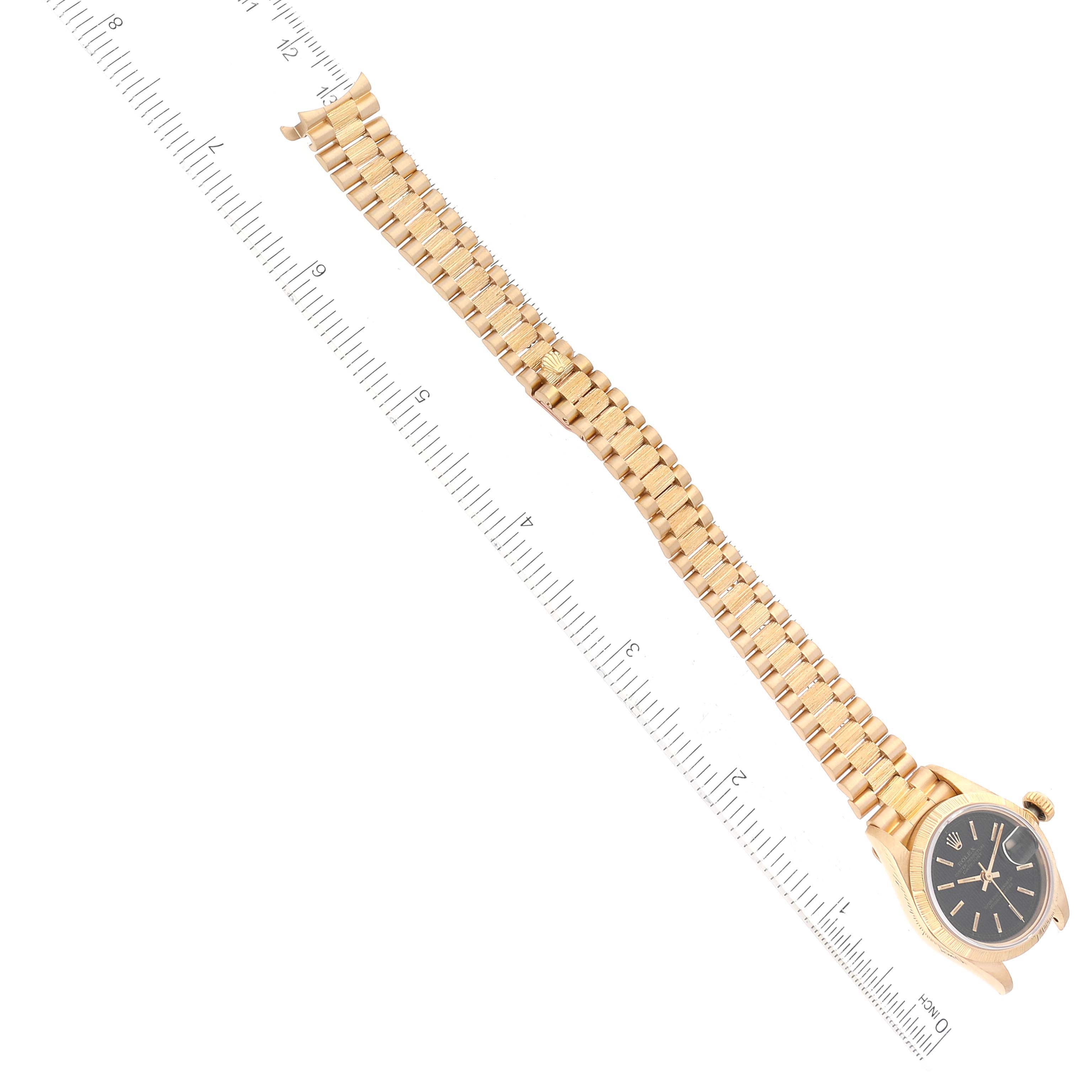 This image shows a Rolex Datejust 69278 Women's Yellow Gold Black Dial 69278 Women's Yellow Gold Black Dial watch laid flat with its gold bracelet extended, alongside a measurement ruler.