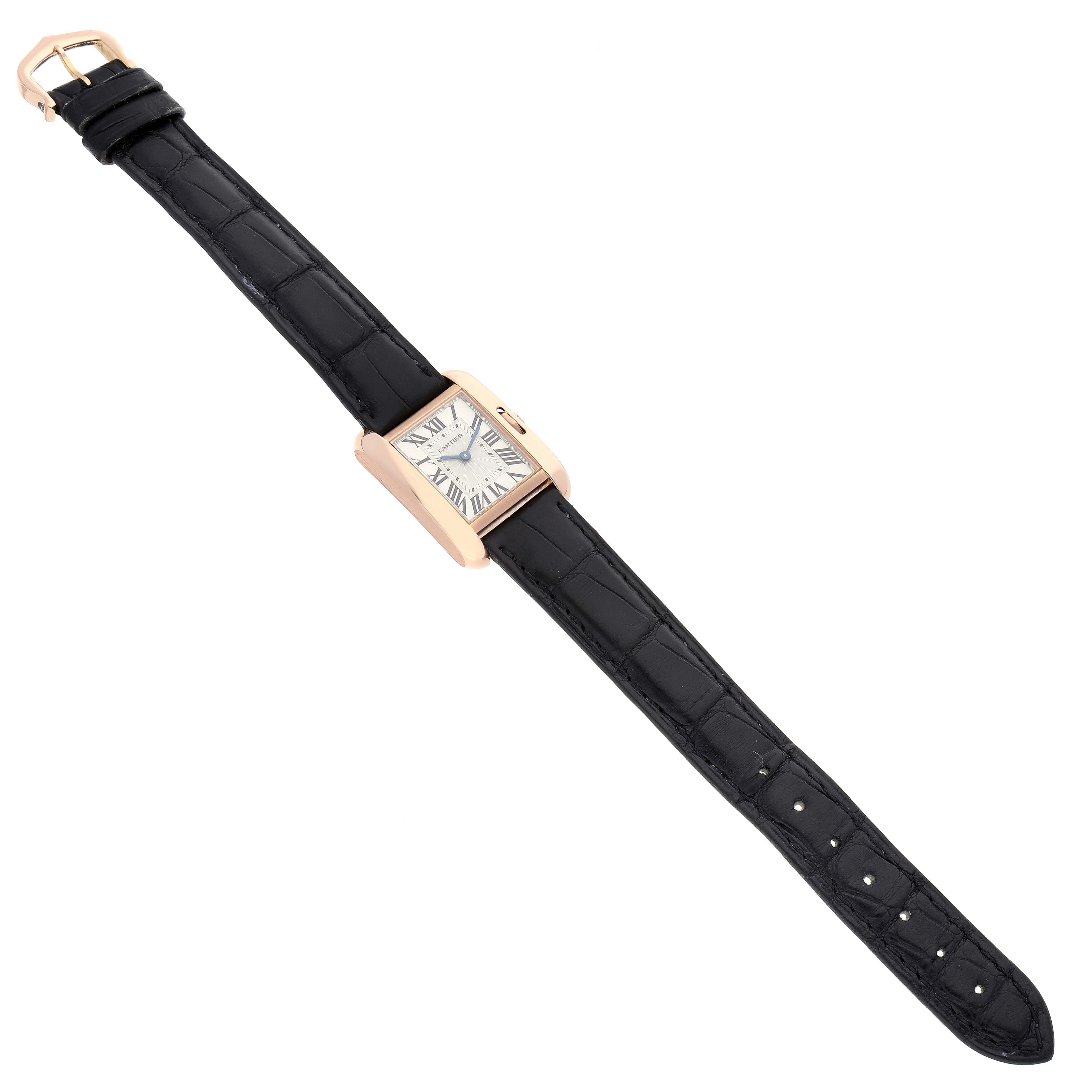 The Cartier Tank Anglaise W5310027 Women
s Rose Gold Silver Dial W5310027 Women
s Rose Gold Silver Dial watch is shown from an aerial view, displaying its black strap and rectangular gold case with the watch face.