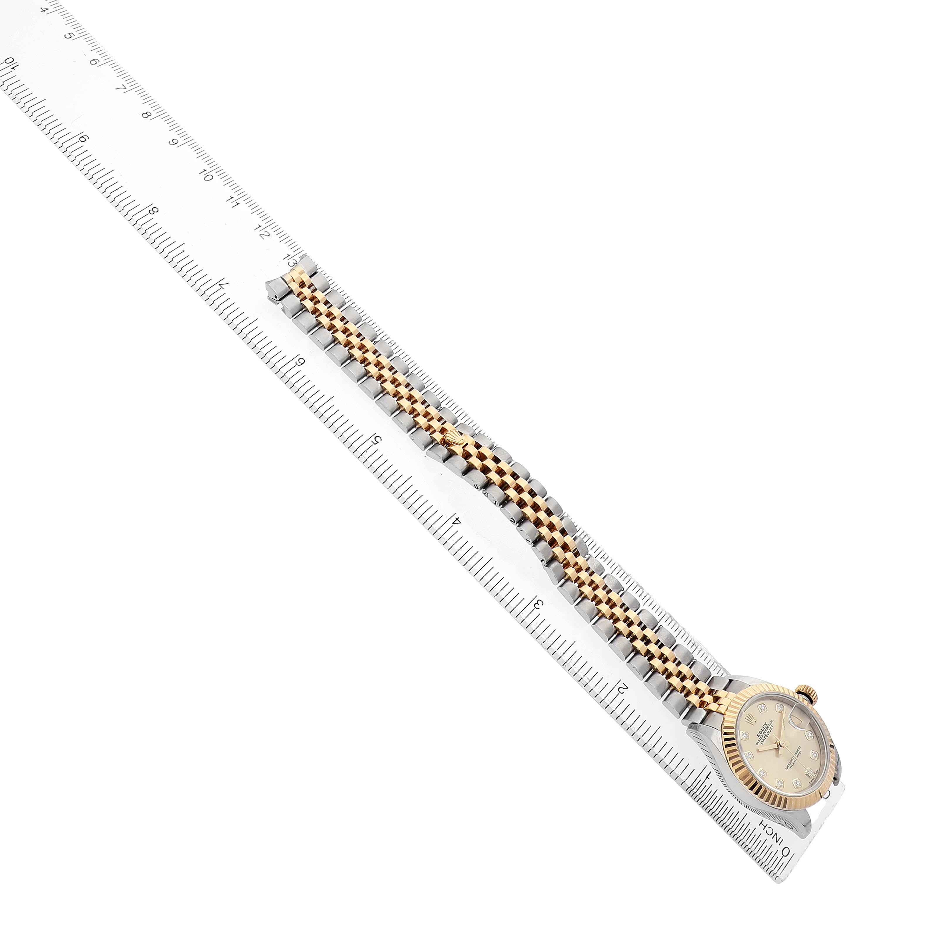 The Rolex Datejust 279173 Women's Steel and Gold (two tone) Champagne Dial watch is shown from a top angle with its dial, bezel, and full bracelet visible alongside a ruler.