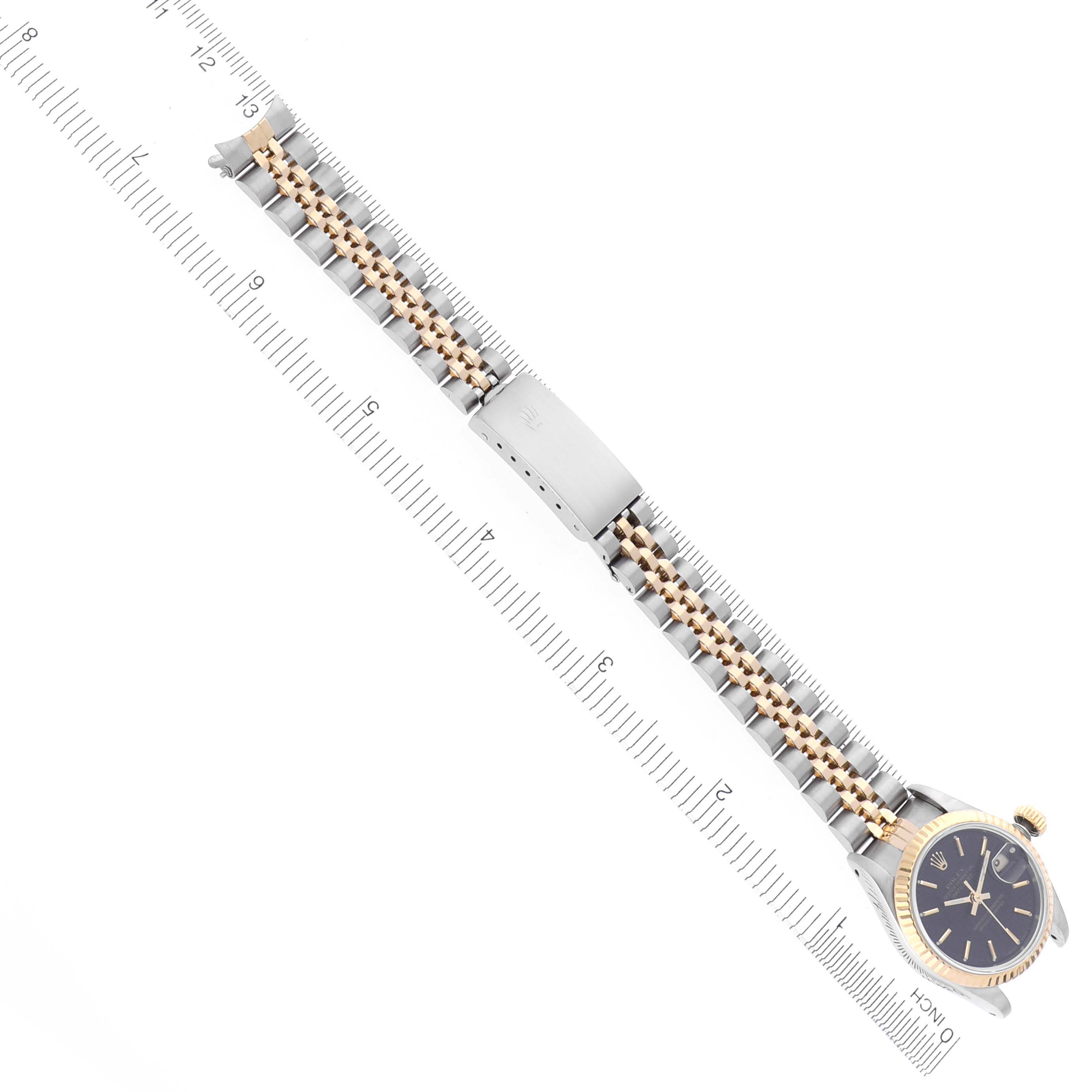 The Rolex Datejust 69173 Women's Steel and Gold (two tone) Black Dial 69173 Women's Steel and Gold (two tone) Black Dial watch is shown from a top-down angle, displaying the face, bezel, and entire bracelet alongside a ruler.