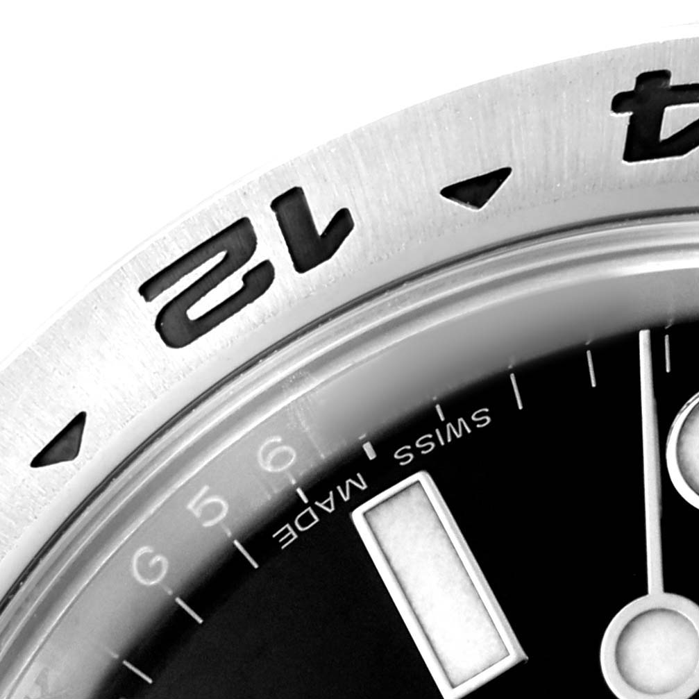 The image shows a close-up of the bezel and part of the dial of a Rolex Explorer 216570 Men's Stainless Steel Black Dial watch, featuring hour markers and numerals.