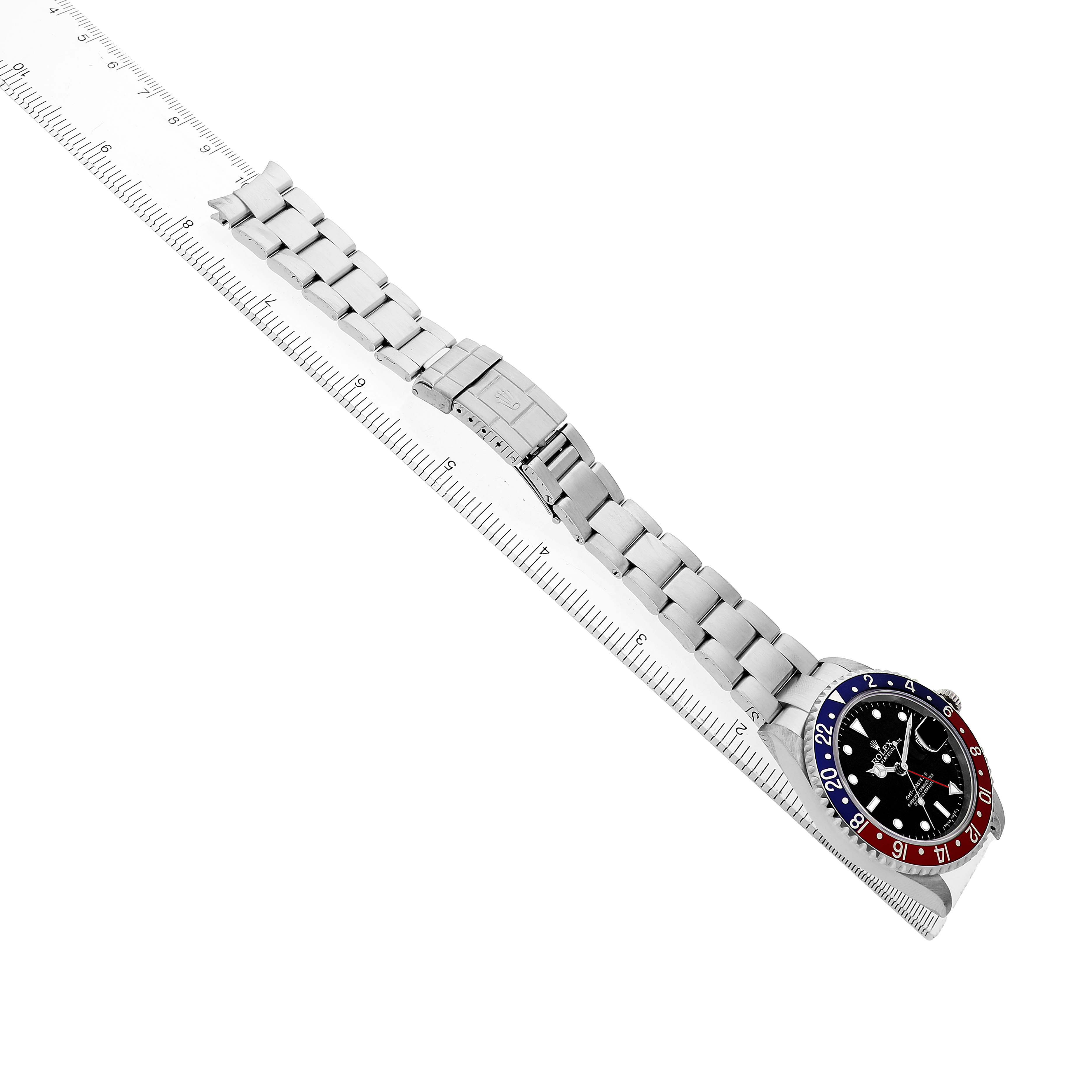 The Rolex GMT-Master 16710 Men's Stainless Steel Black Dial watch is shown angled sideways, displaying its face, bezel, and stainless steel bracelet resting on a ruler.