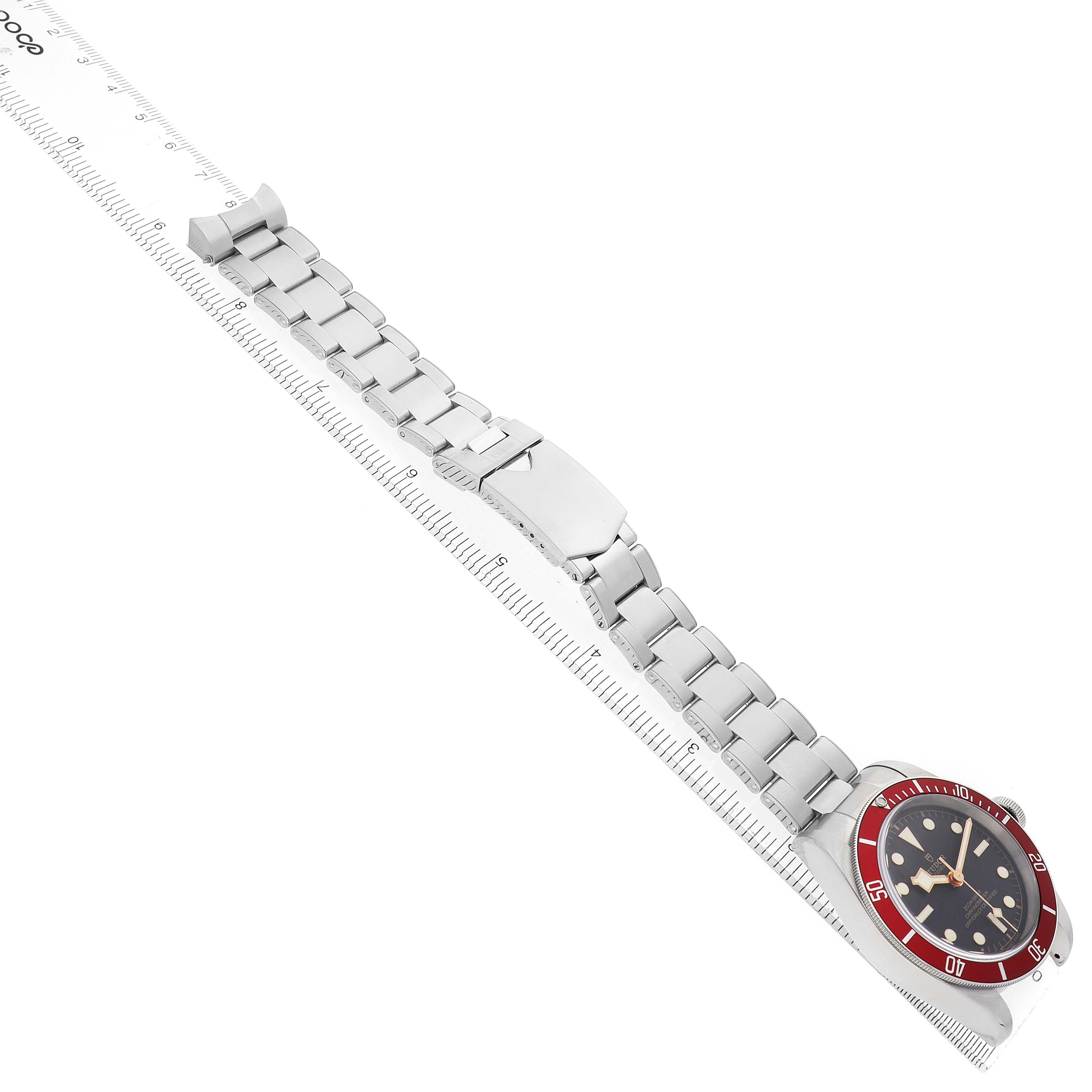 The Tudor Heritage Black Bay 79230R-0003 Men's Stainless Steel Black Dial watch is shown at an angle showcasing the full bracelet, clasp, and face with a red bezel.