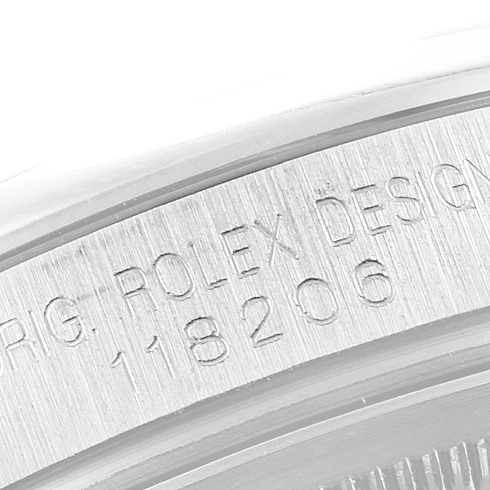 The image shows the edge of a Rolex President 118206 Men's Platinum Silver Dial 118206 Men's Platinum Silver Dial model watch case, featuring engraved design markings and the serial number.