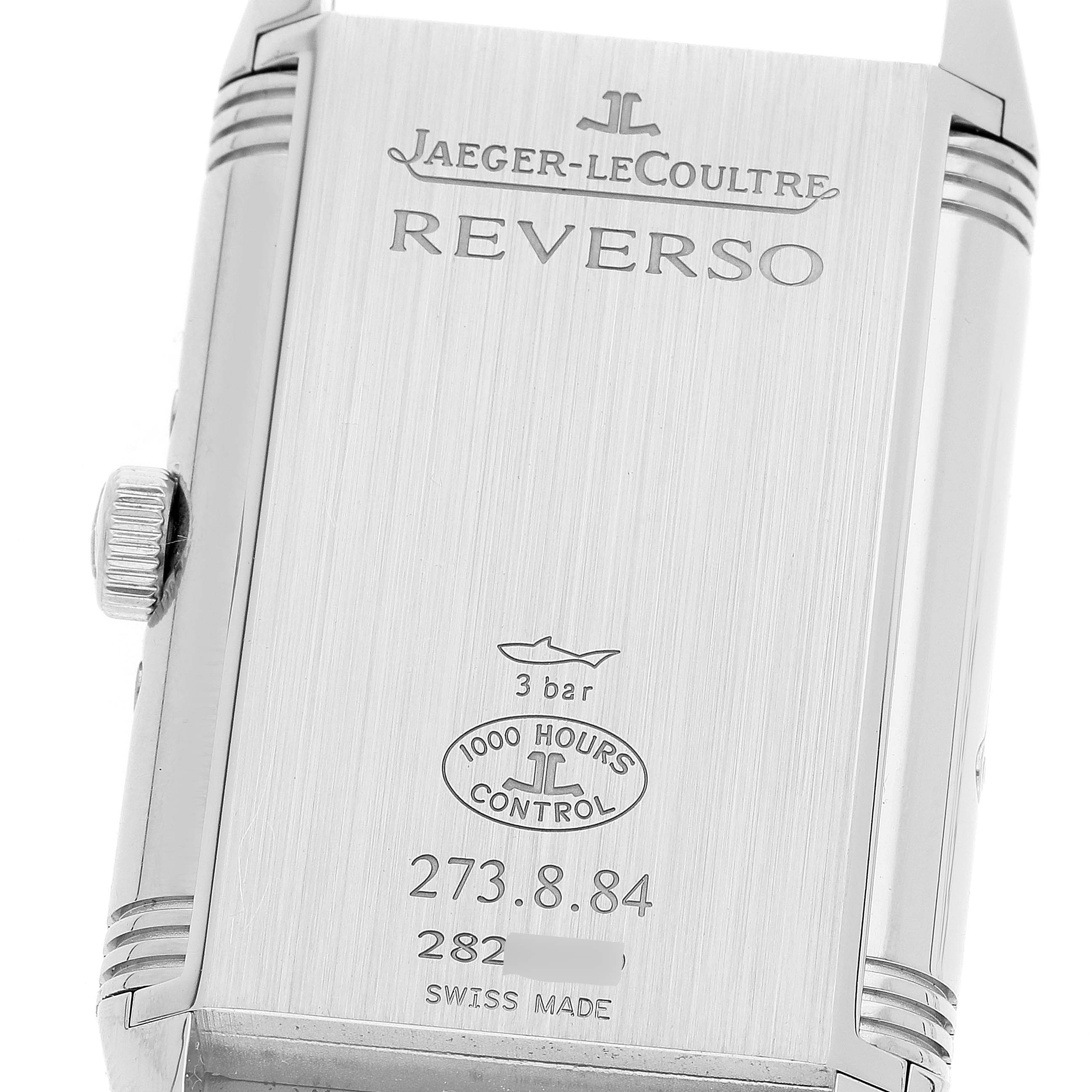 The image shows the back of a Jaeger-LeCoultre Reverso watch, featuring engraving and the crown.