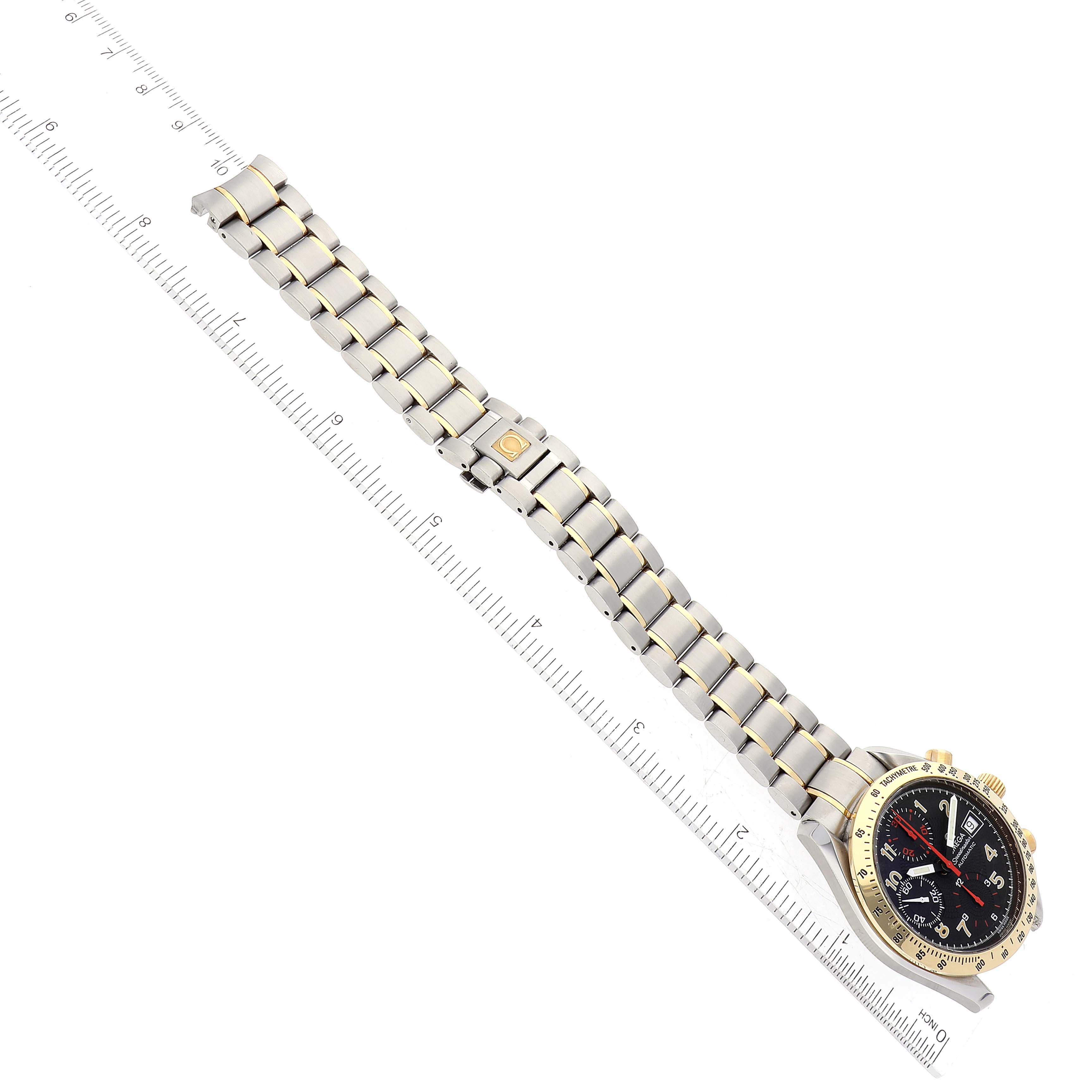 This image shows an Omega Speedmaster 3313.53.00 Men's Steel and Gold (two tone) Black Dial 3313.53.00 Men's Steel and Gold (two tone) Black Dial watch laid flat, including the face, case, and full bracelet, angled slightly with a ruler beside it.