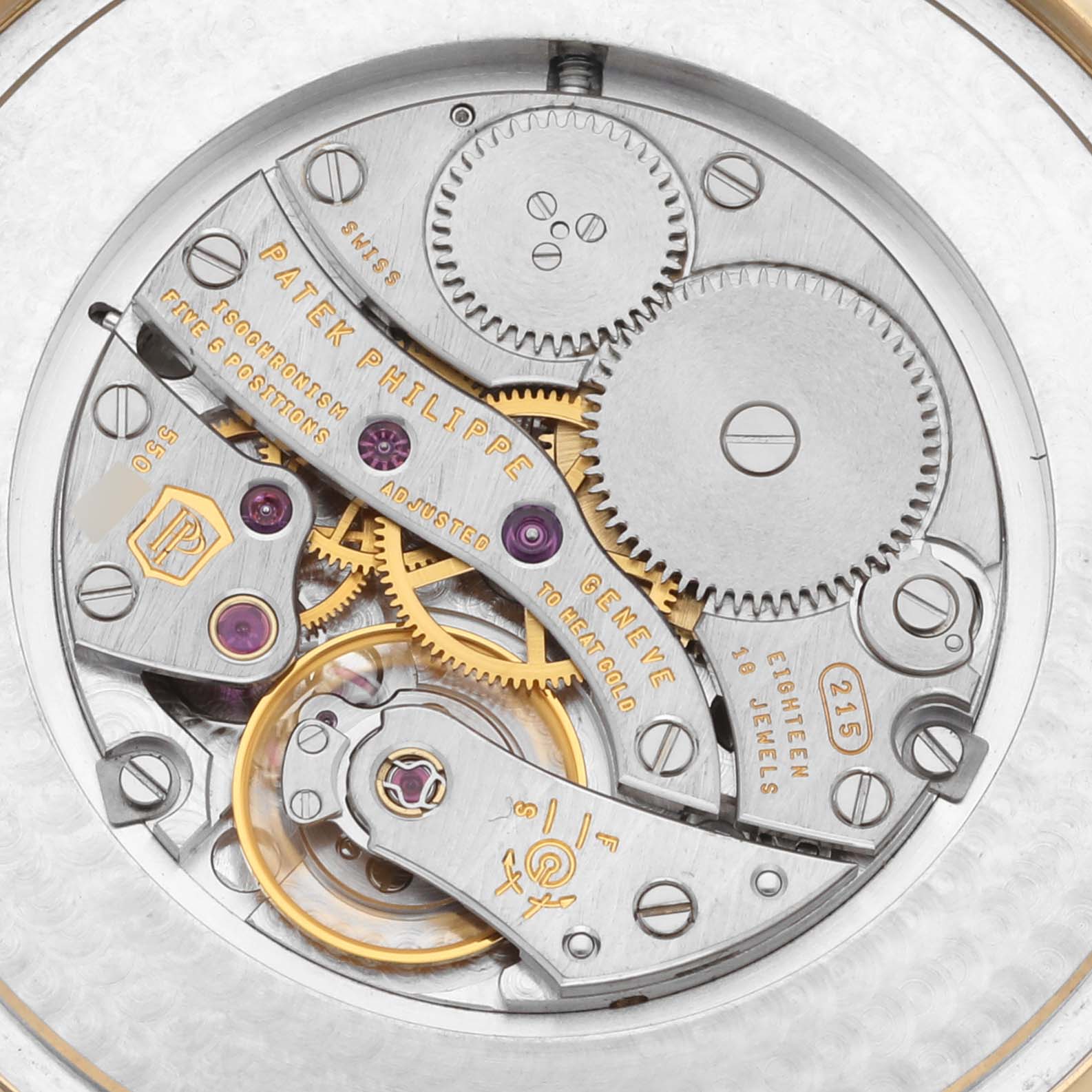 The image shows the intricate movement of the Patek Philippe Calatrava 5196J-001 Men's Yellow Gold Silver Dial 5196J-001 Men's Yellow Gold Silver Dial watch from a top-down angle, highlighting gears and inscriptions.