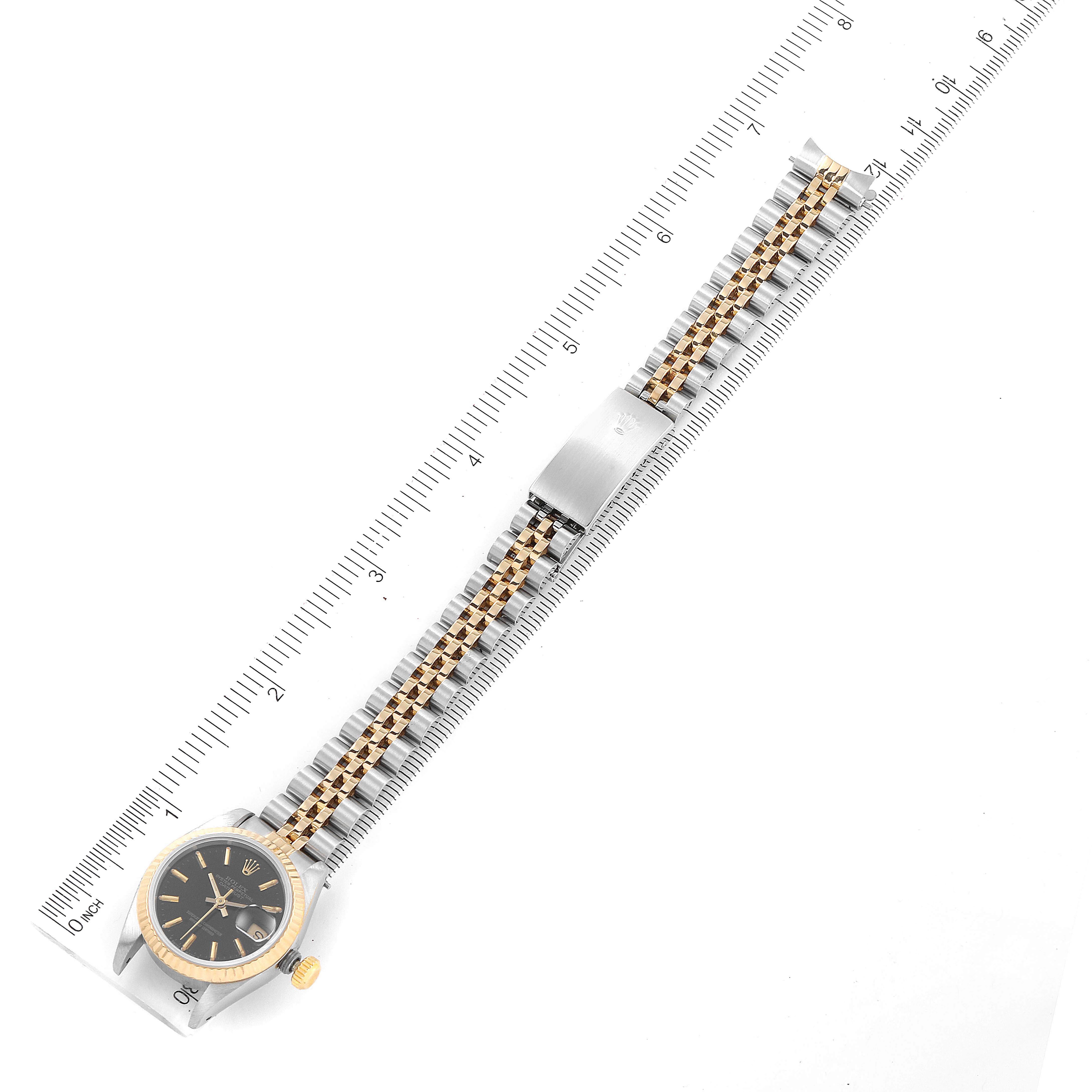 The Rolex Datejust 69173 Women's Steel and Gold (two tone) Black Dial 69173 Women's Steel and Gold (two tone) Black Dial watch is shown lying flat under a ruler, displaying the dial, bezel, and bracelet with clasp.