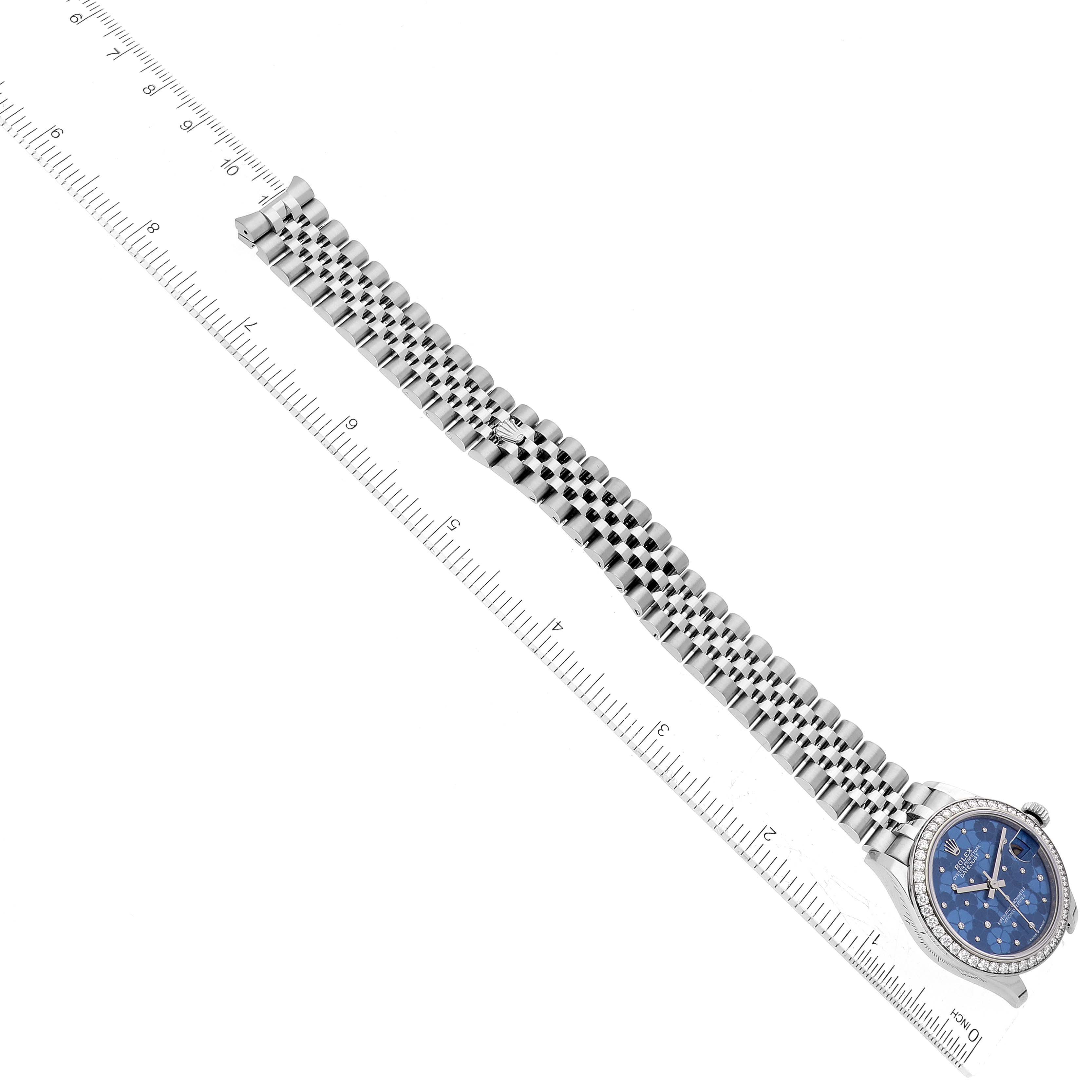 The image shows a Rolex Mid-Size 278384 Women
s Stainless Steel Blue Dial 278384 Women
s Stainless Steel Blue Dial watch from a top-down angle, featuring the band, face, and bezel alongside a measuring ruler.