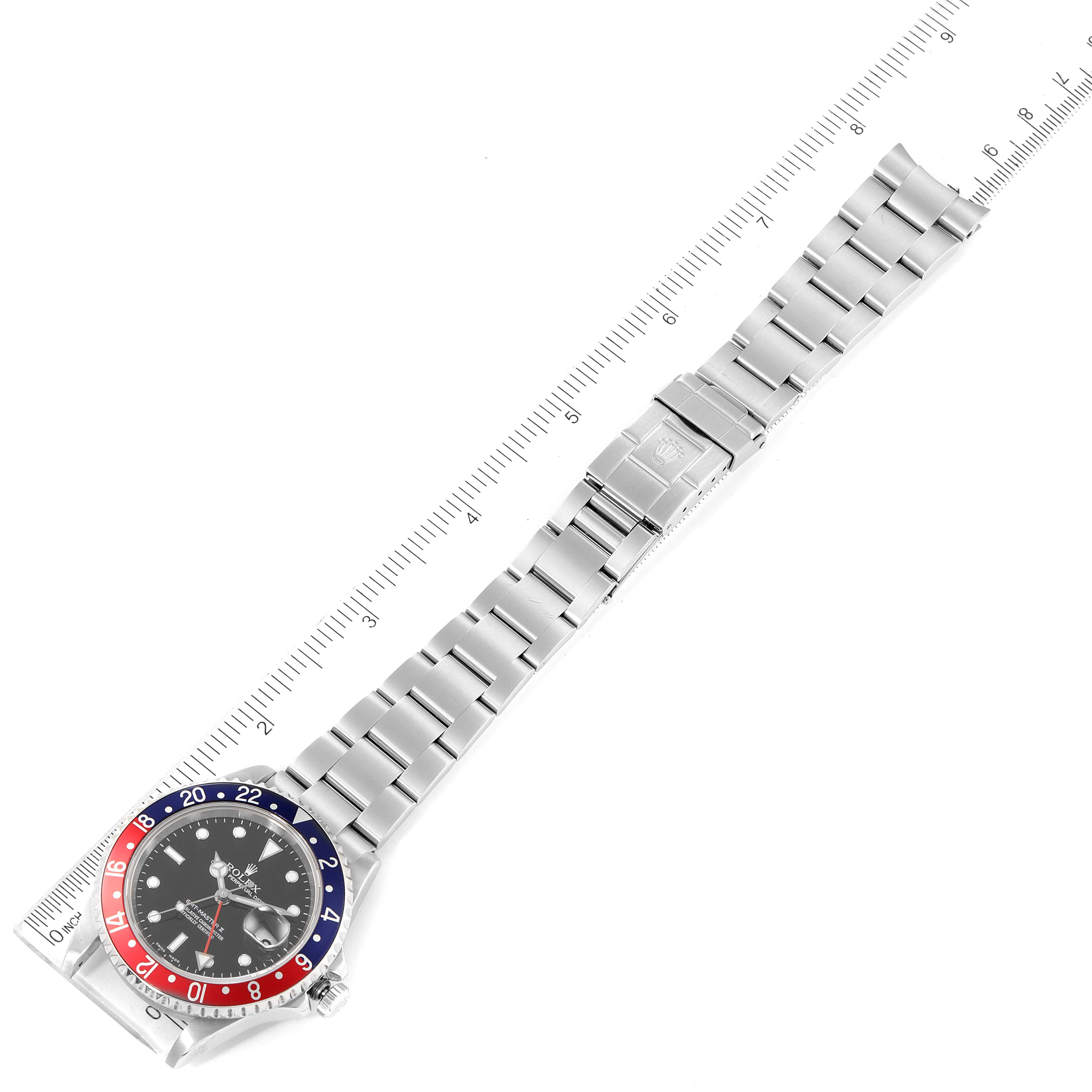The image shows a top-down view of a Rolex GMT-Master 16710 Men's Stainless Steel Black Dial 16710 Men's Stainless Steel Black Dial watch, featuring its face, bezel, and metal bracelet with a ruler for scale.