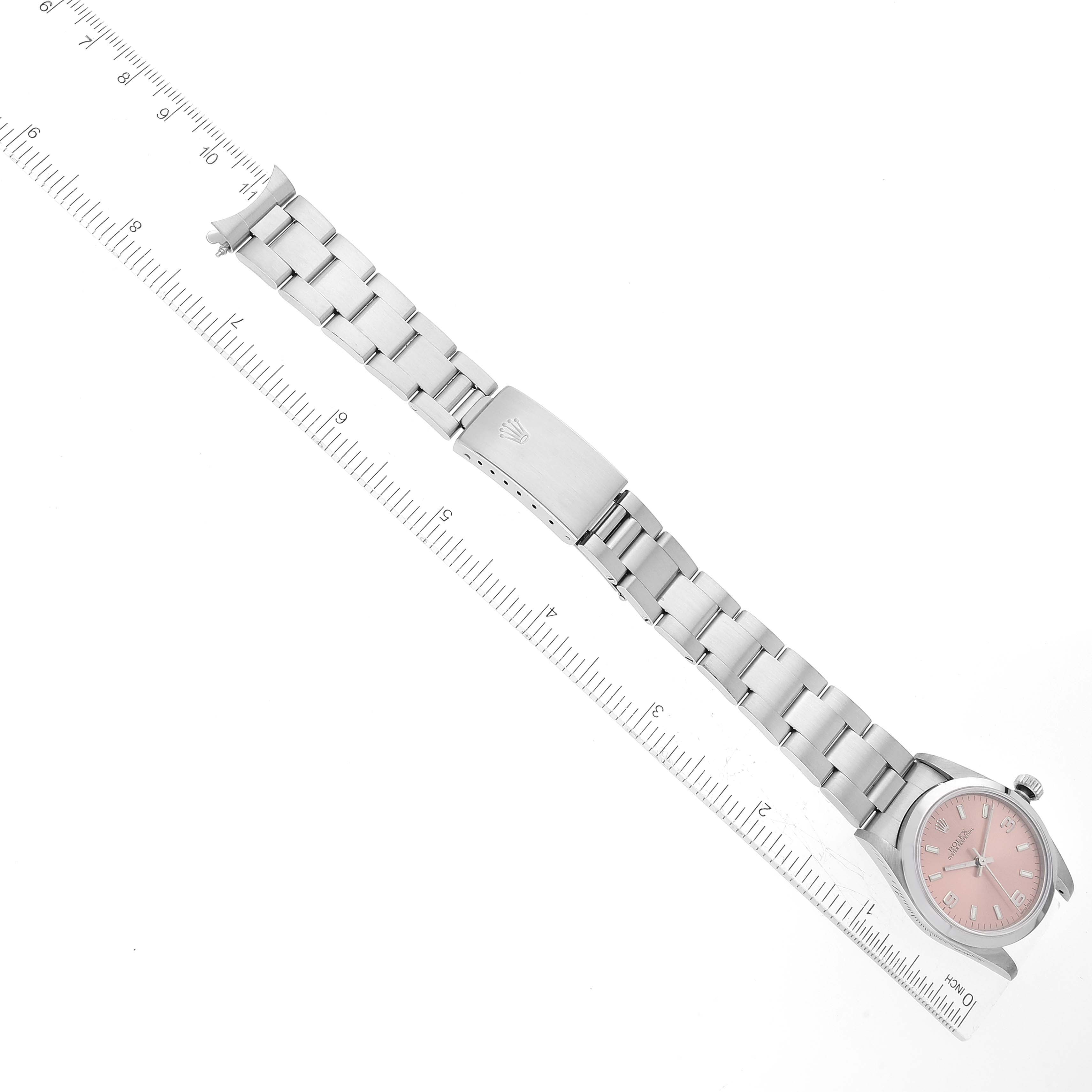 The image shows a top view of a Mid-Size Rolex watch with a pink dial, stainless steel bracelet, and clasp, alongside a ruler for scale.