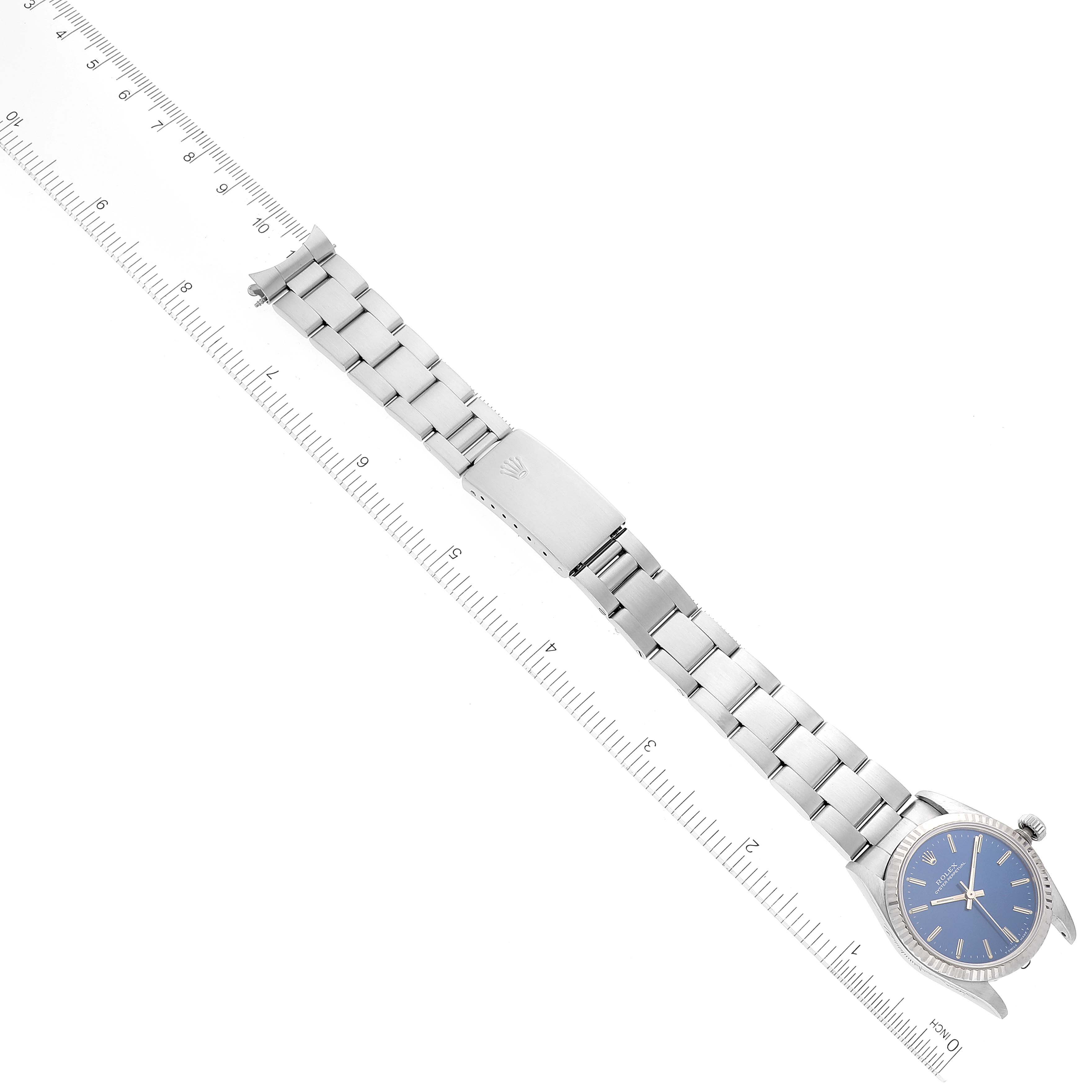 This image shows a Mid-Size Rolex watch with a blue dial and stainless steel bracelet, laid flat alongside a ruler.