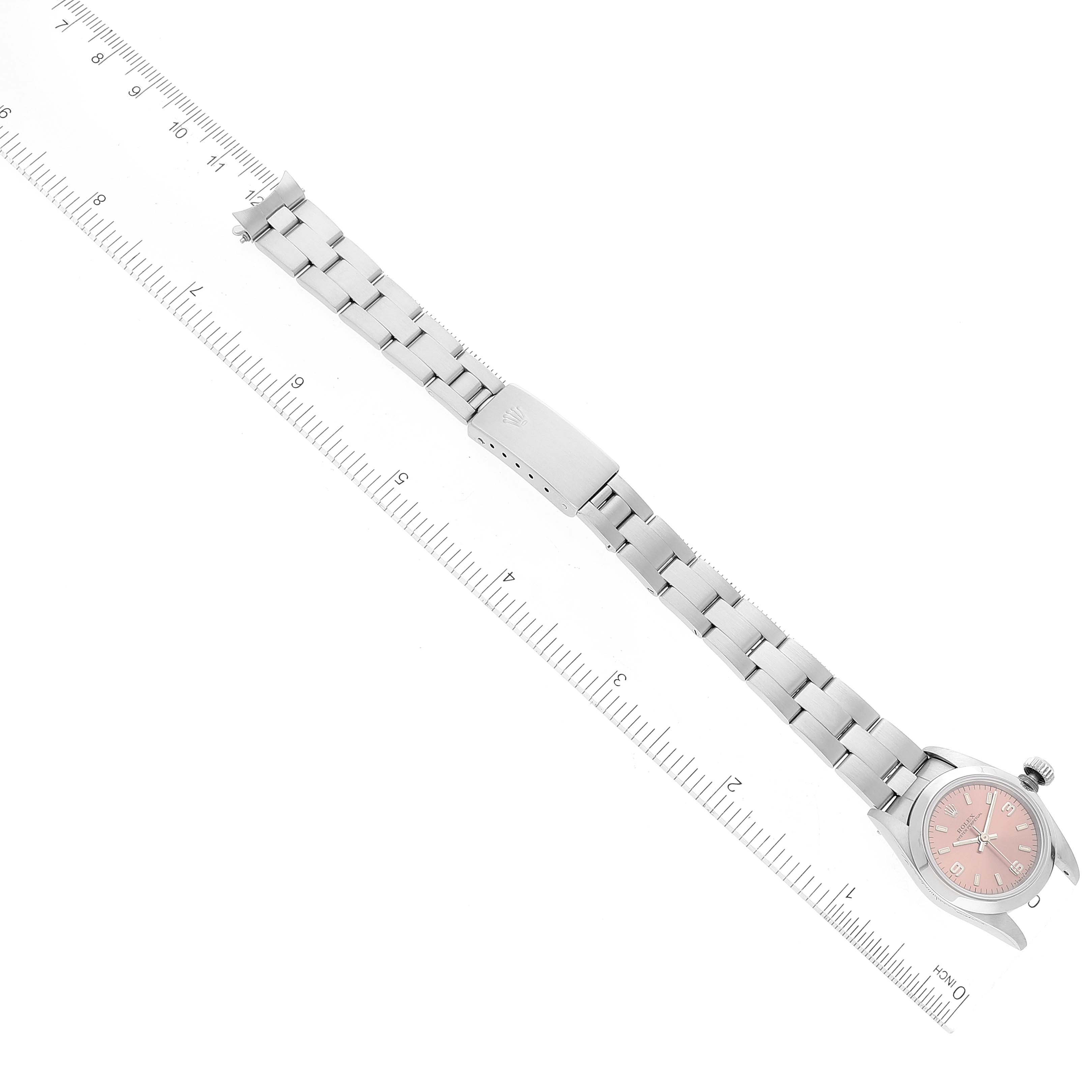 The image shows a top-down view of a Rolex Oyster Perpetual 67180 Women
s Stainless Steel Pink Dial 67180 Women
s Stainless Steel Pink Dial watch with a pink dial alongside a ruler to display its length.