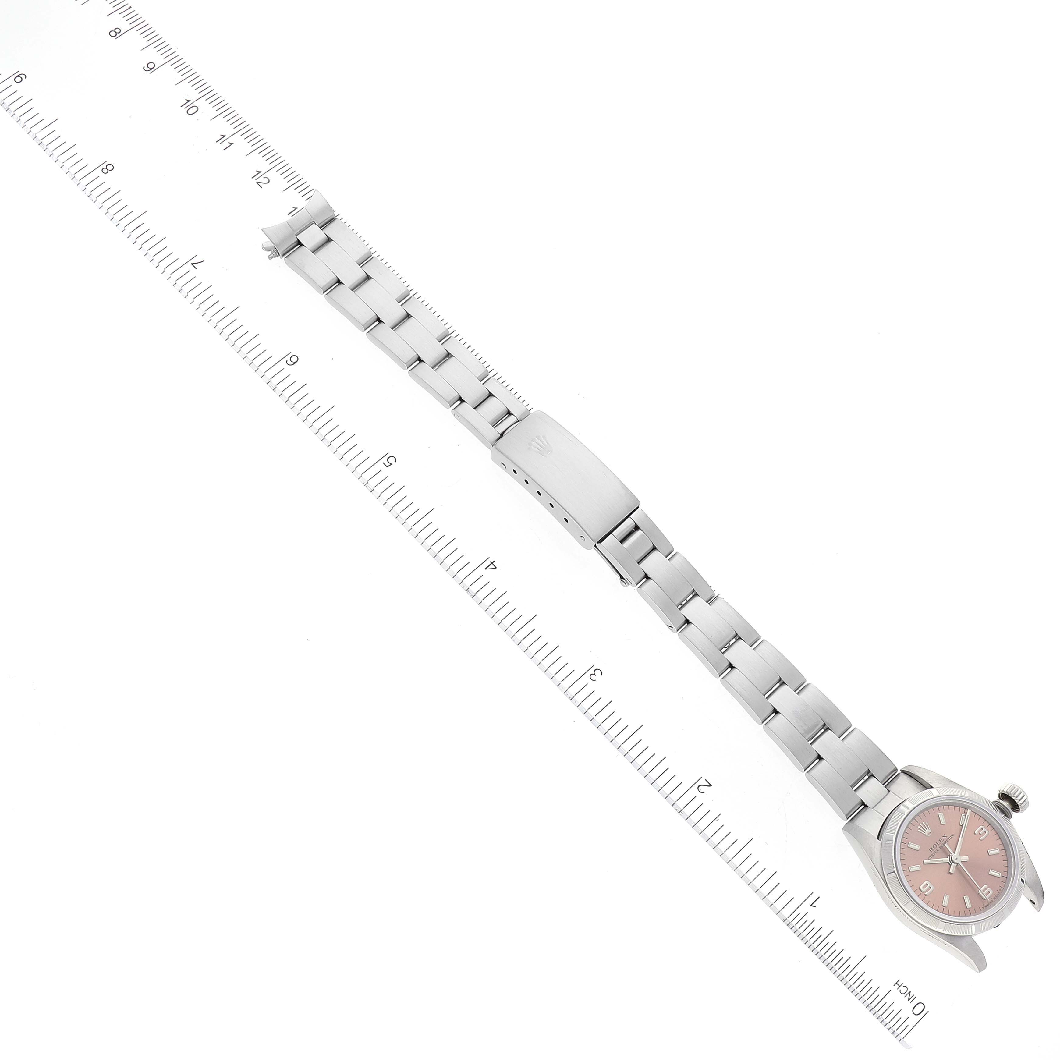 The image shows a Rolex Oyster Perpetual 67230 Women
s Stainless Steel Pink Dial 67230 Women
s Stainless Steel Pink Dial watch laid flat with the full bracelet and clasp visible against a ruler for scale.