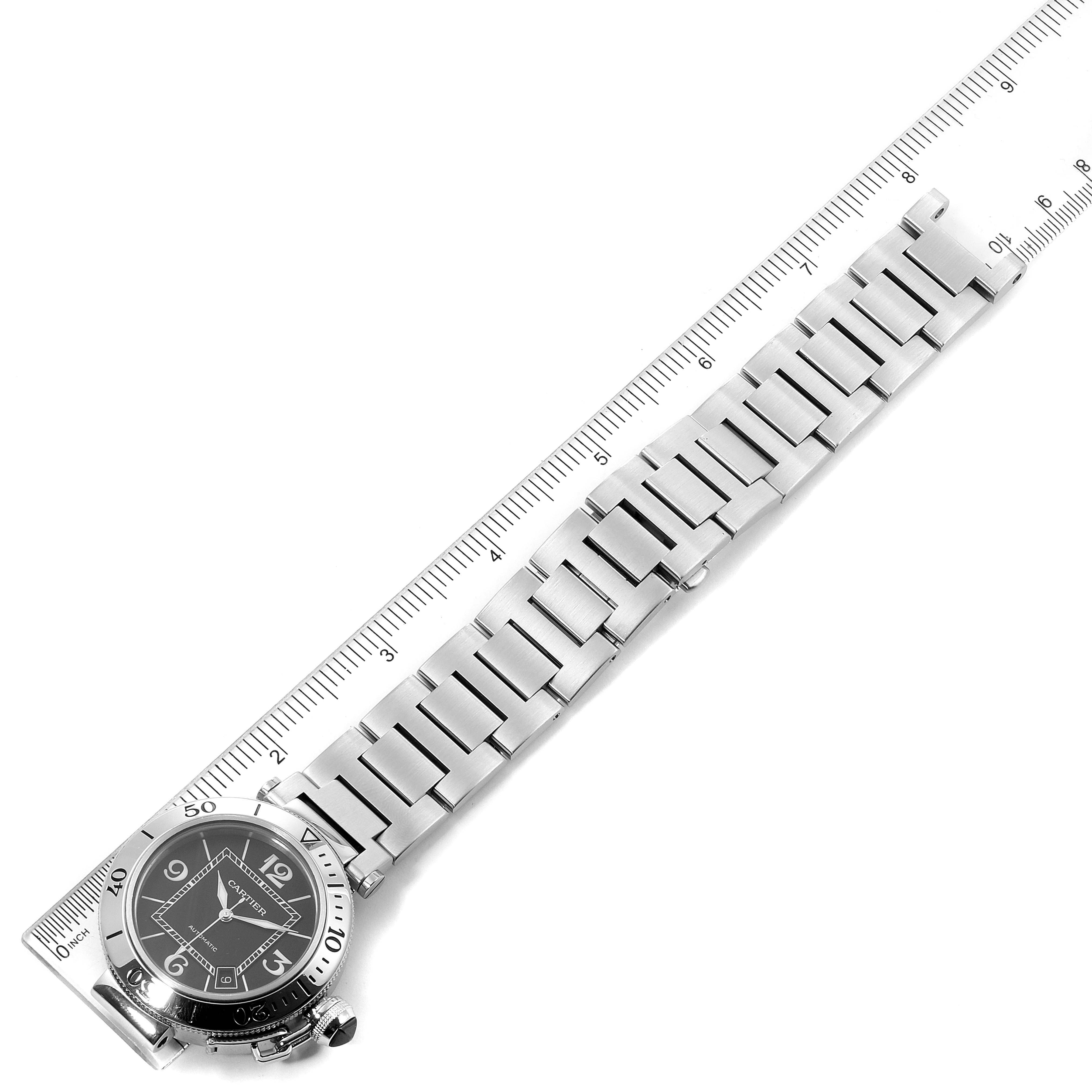The image shows the Cartier Pasha W31077M7 Men's Stainless Steel Black Dial W31077M7 Men's Stainless Steel Black Dial watch from a top-down angle, highlighting its dial, bezel, and metal bracelet against a ruler.