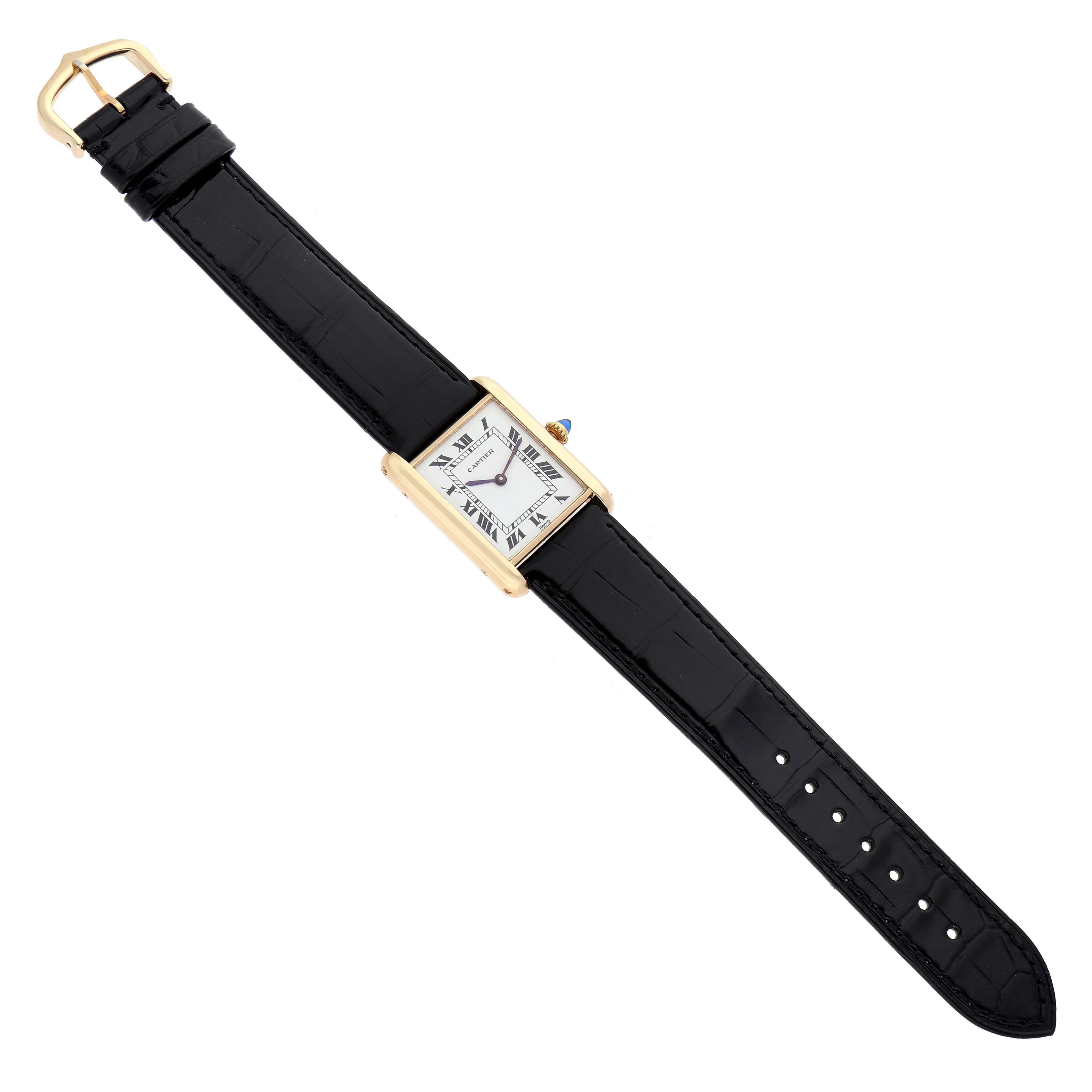 The Cartier Tank Classic Women's Yellow Gold White Dial watch is shown from a top-down angle, displaying the gold rectangular case, white dial, and black leather strap.