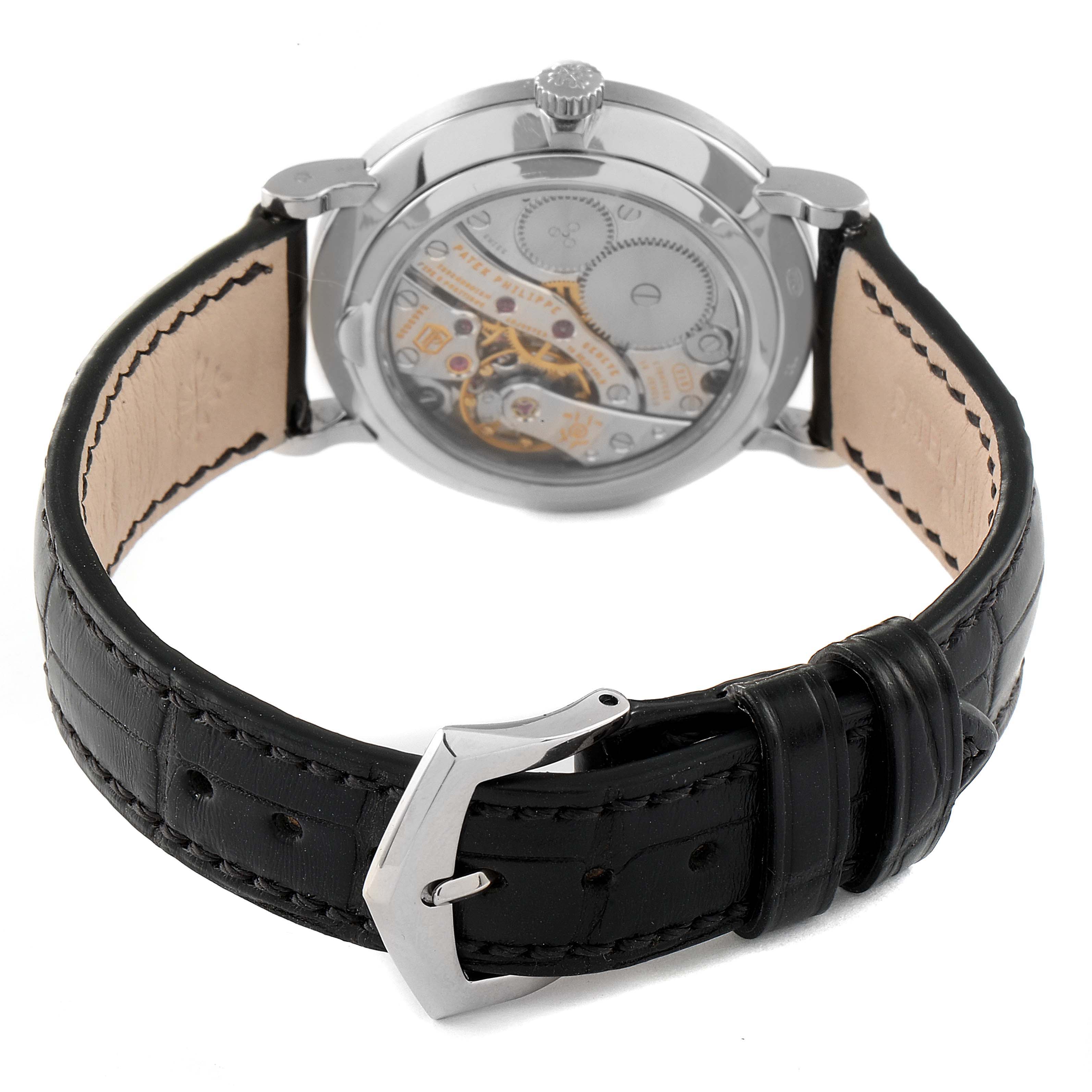 The image shows the back view of a Patek Philippe Calatrava 7119G Women's White Gold White Dial 7119G Women's White Gold White Dial watch, highlighting its movement and black leather strap with a buckle.