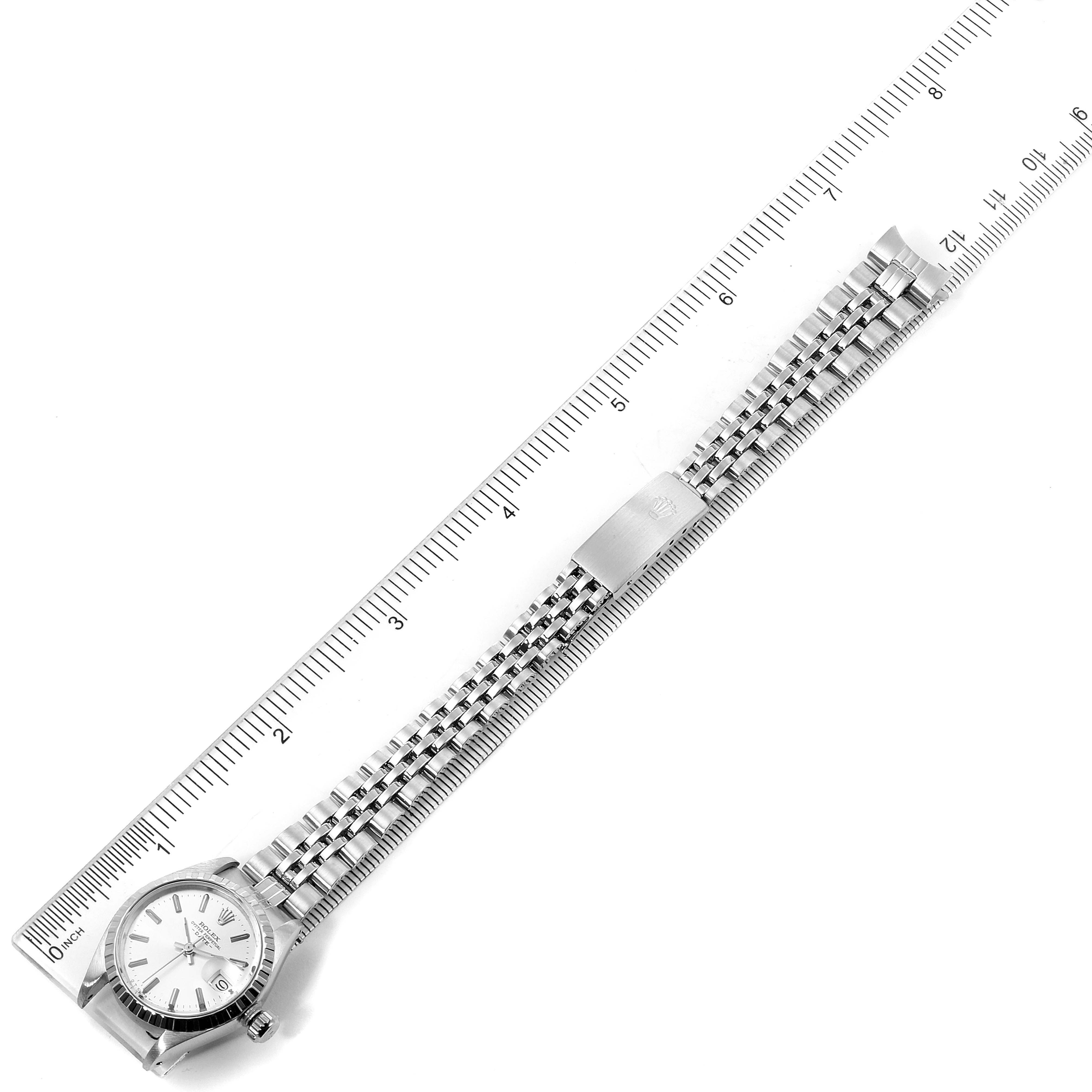 The image shows a top-down view of a Rolex Date 6924 Women
s Stainless Steel Silver Dial 6924 Women
s Stainless Steel Silver Dial model watch alongside a ruler, displaying the dial, bracelet, and clasp.